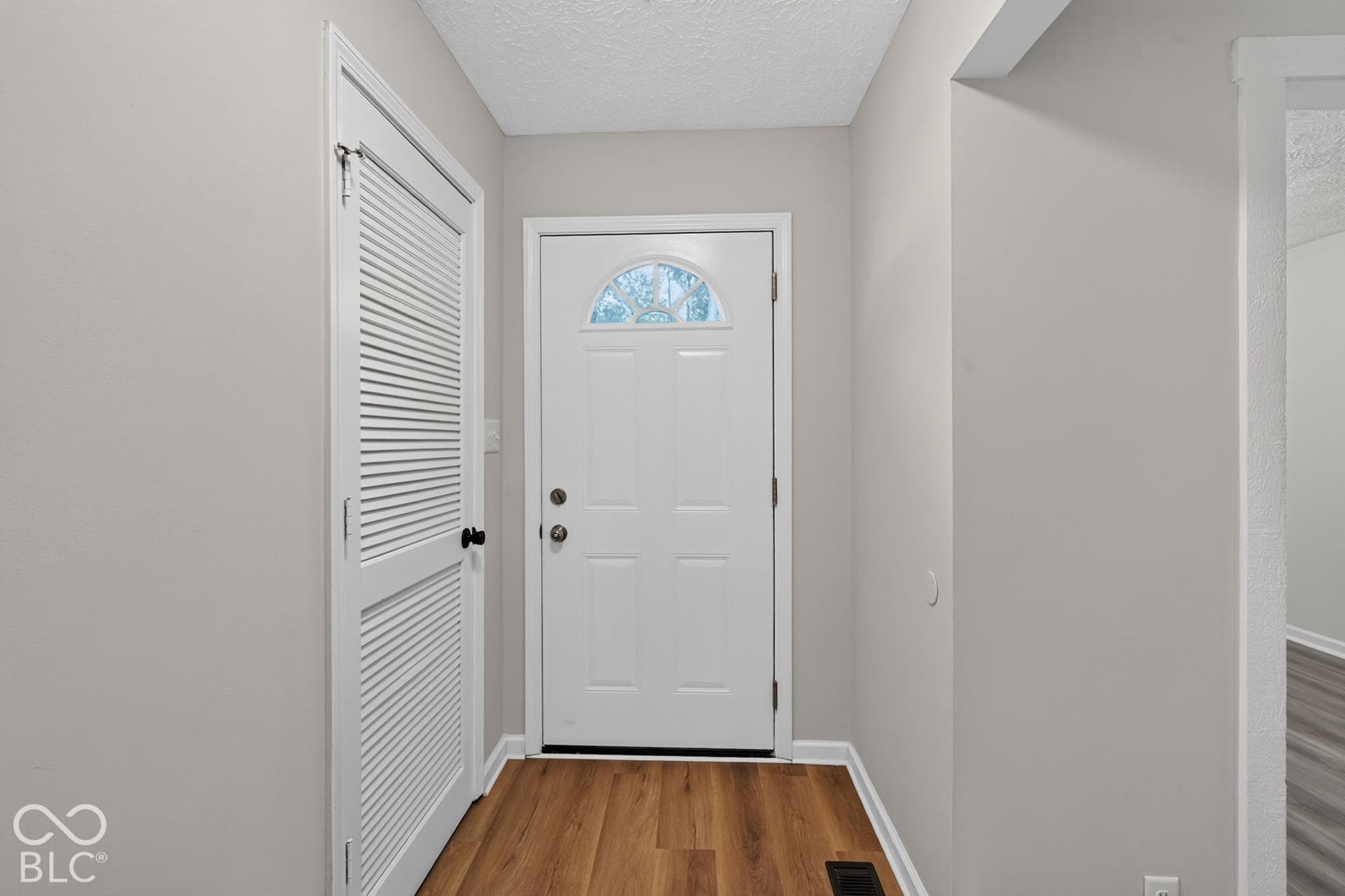 Entryway with wood-finish flooring and a white front door featuring a decorative transom window