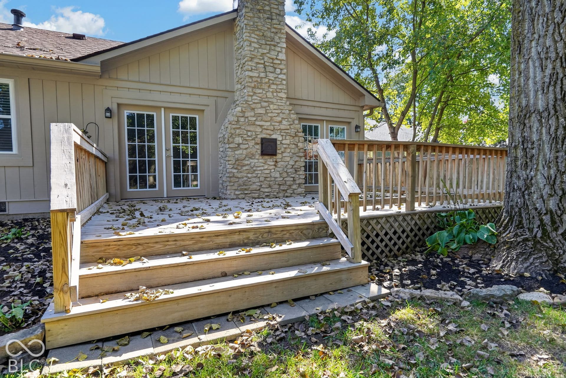 Expansive wooden deck with railing, stairs, and lattice skirting, featuring stone chimney exterior and double glass panel doors
