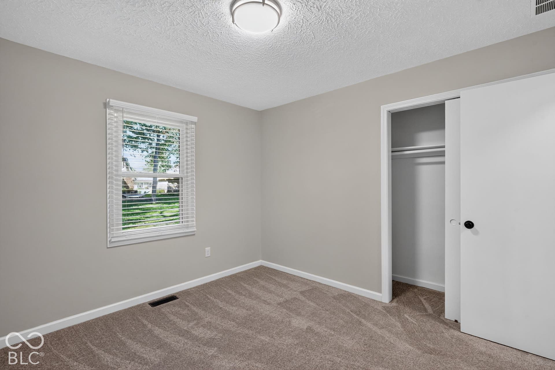 Neutral tone wall color, carpeted flooring, window with blinds, and a built-in closet with sliding doors