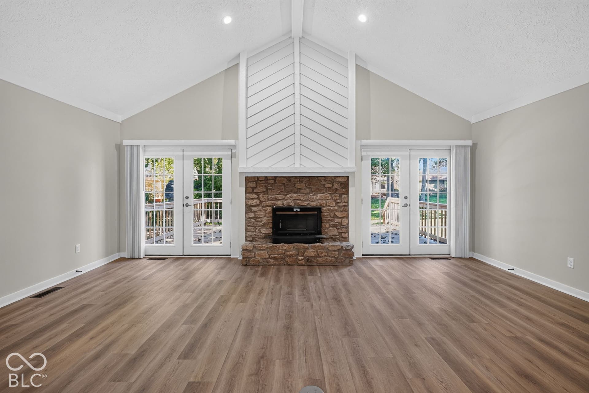 Vaulted ceiling with exposed beams, wood-finish flooring, stone fireplace, and two sets of glass French doors