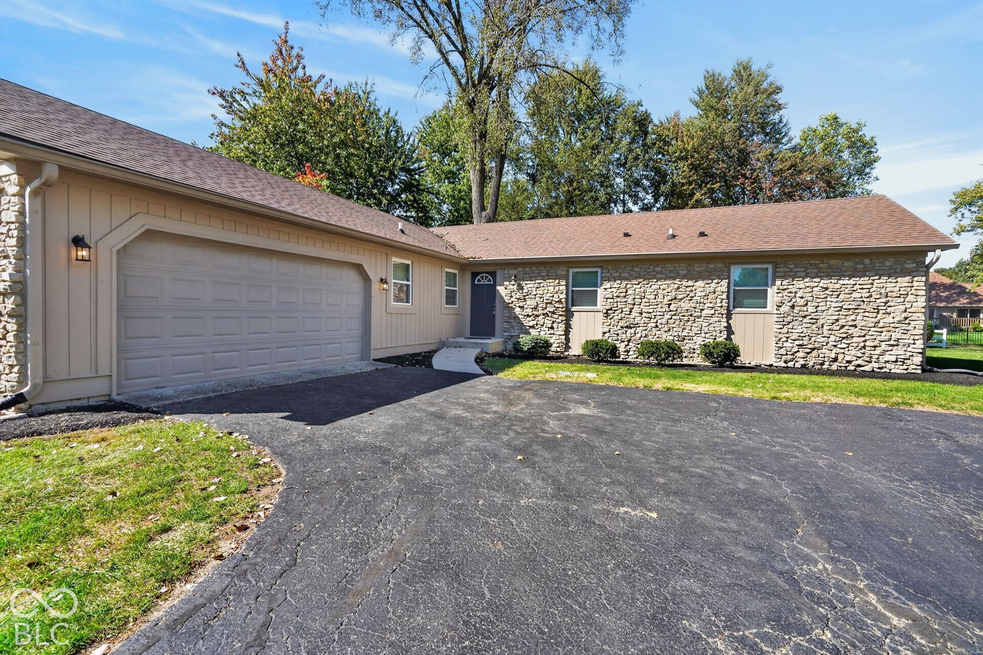 Exterior with stone facade, beige siding, a two-car garage, and a paved driveway