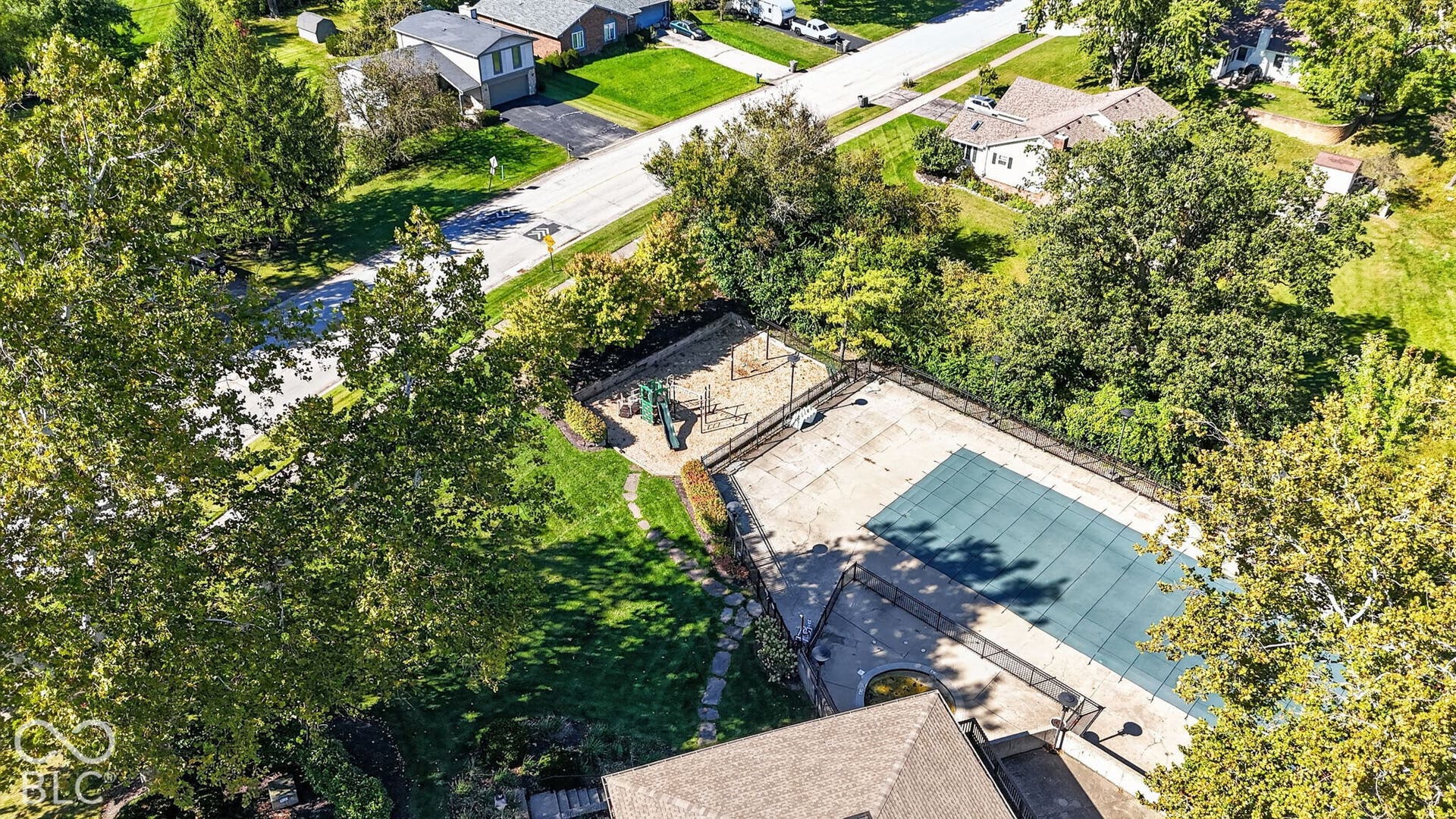 Outdoor swimming pool with a covered surface, surrounded by a concrete patio and a dark metal fence