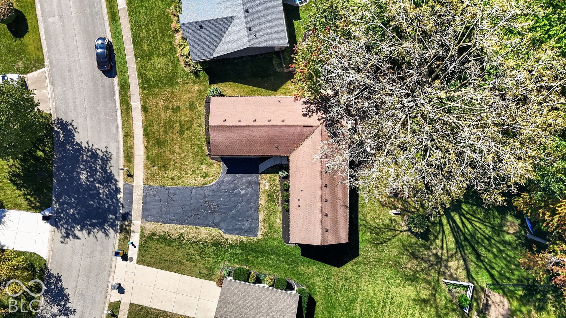 Gable roofline, asphalt shingle roofing, paved driveway, mature trees, and a well-maintained lawn