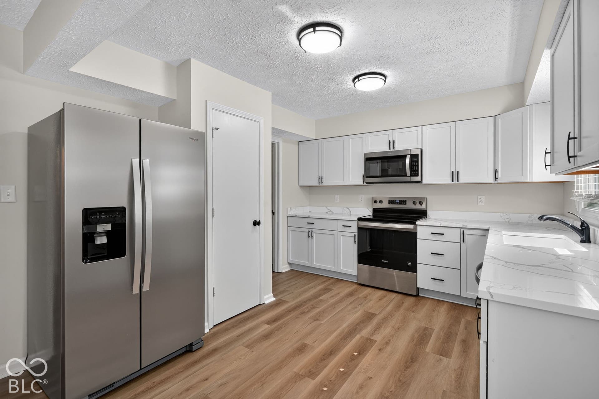 Kitchen featuring wood-finish flooring, white cabinetry, stainless steel appliances, and white countertops