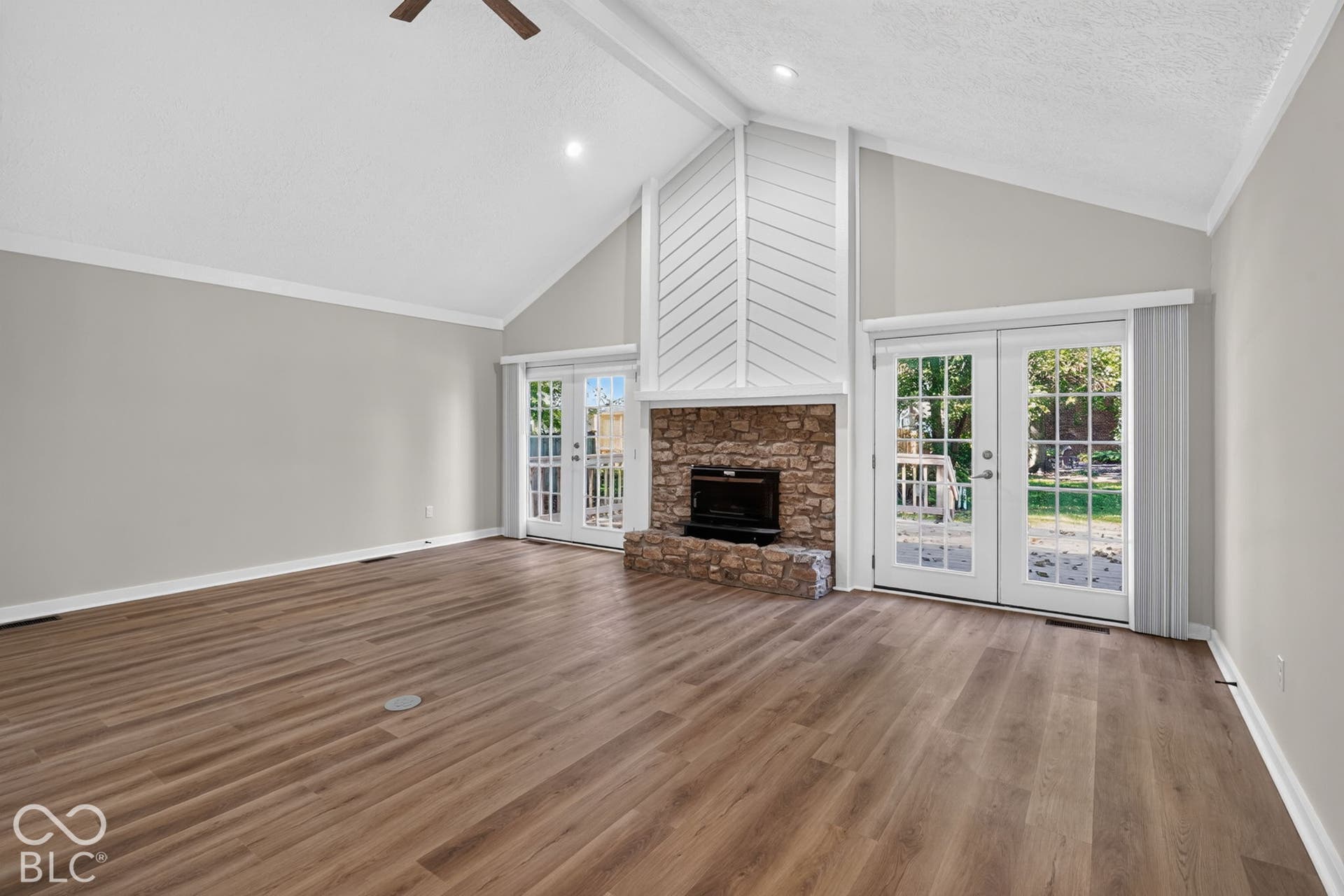 Wood-finish flooring throughout, vaulted ceiling, recessed lighting, stone fireplace, and double French doors