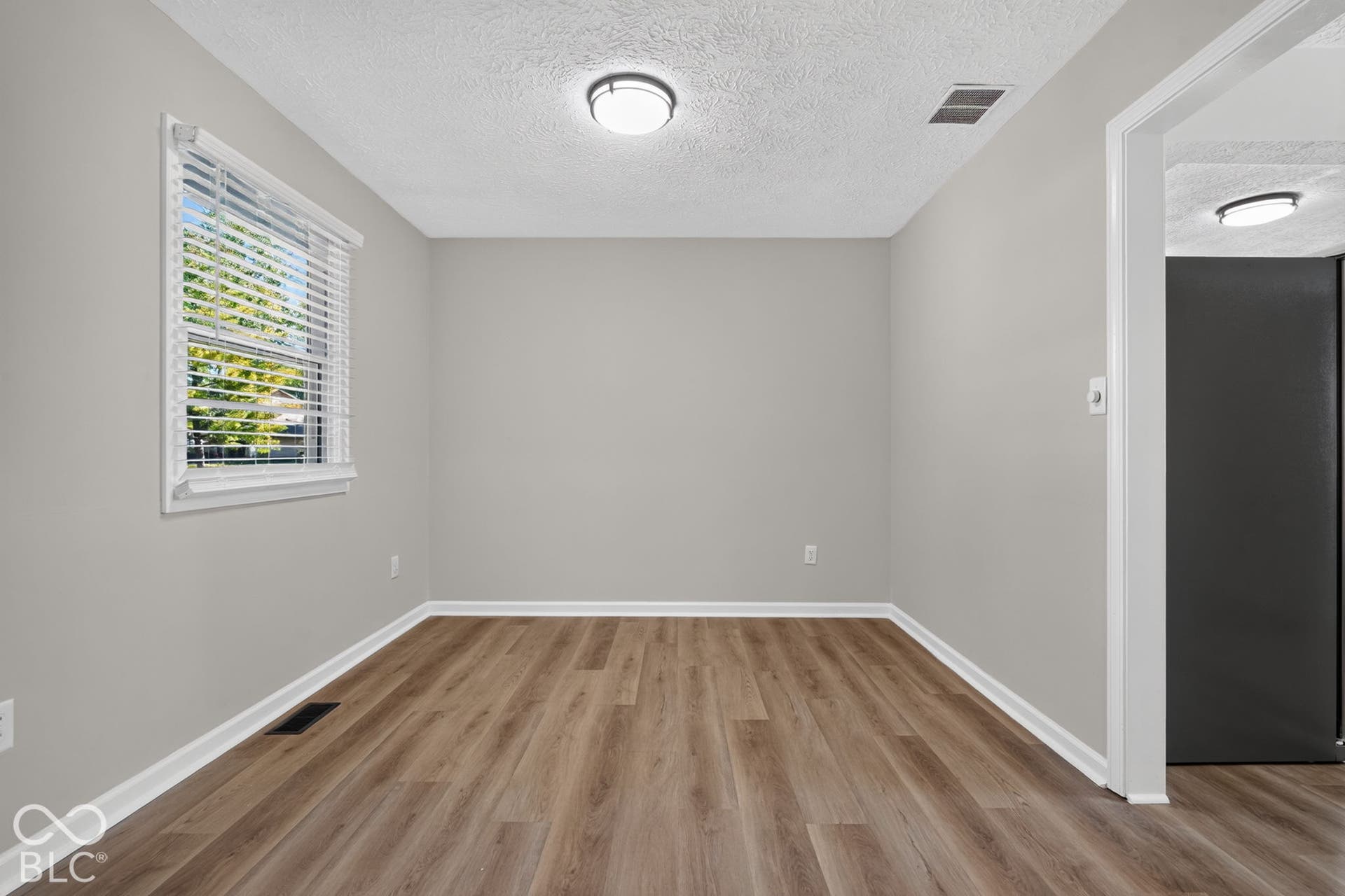 Wood-finish flooring, neutral wall tones, window with horizontal blinds, flush mount ceiling fixture, and a white trim package