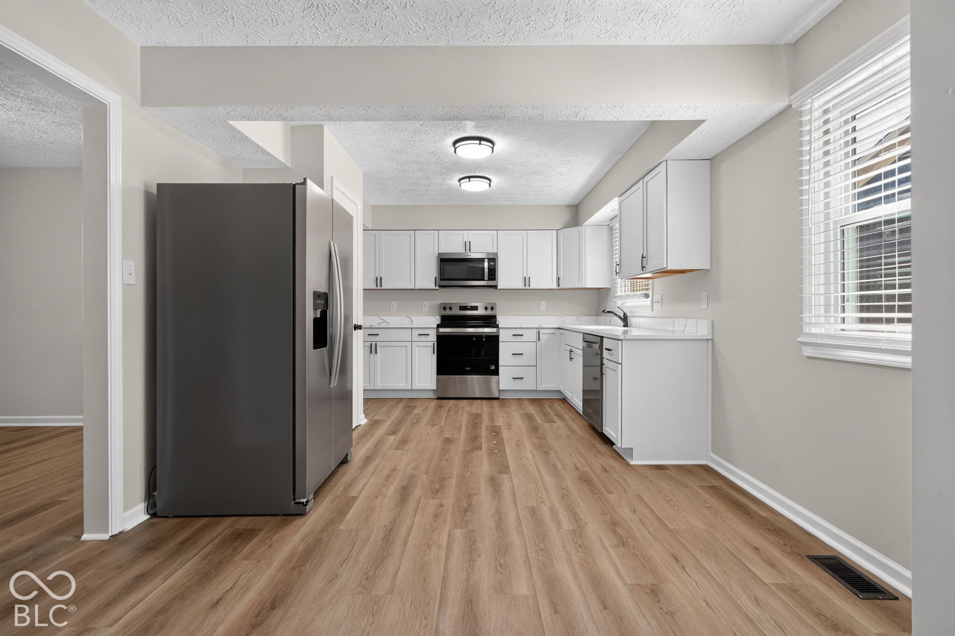 Open-concept kitchen featuring white cabinetry, stainless steel appliances, wood-finish flooring, and a window with blinds