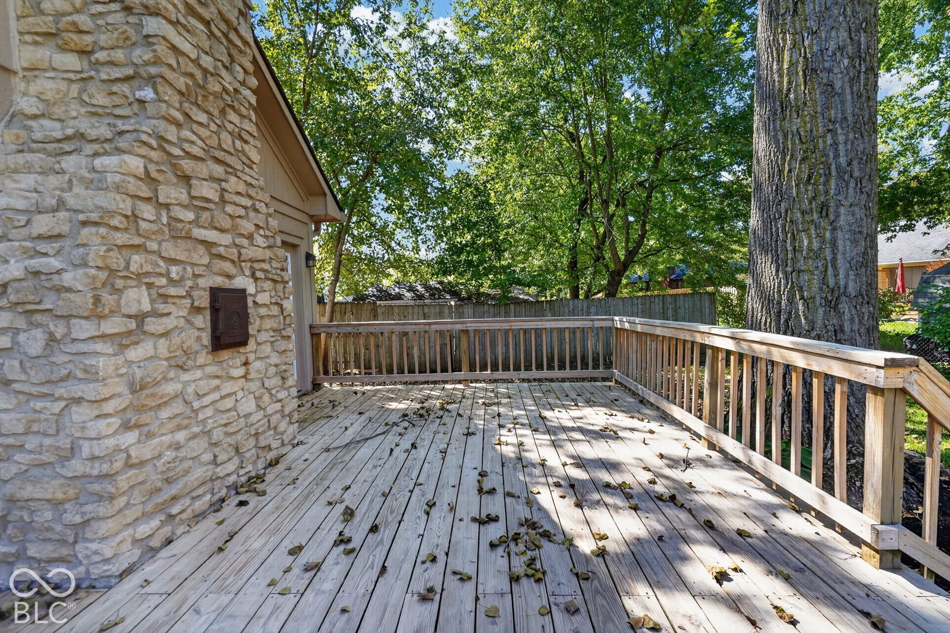 Expansive wood deck with wood railings, adjacent to a natural stone veneer exterior with a built-in metal access panel
