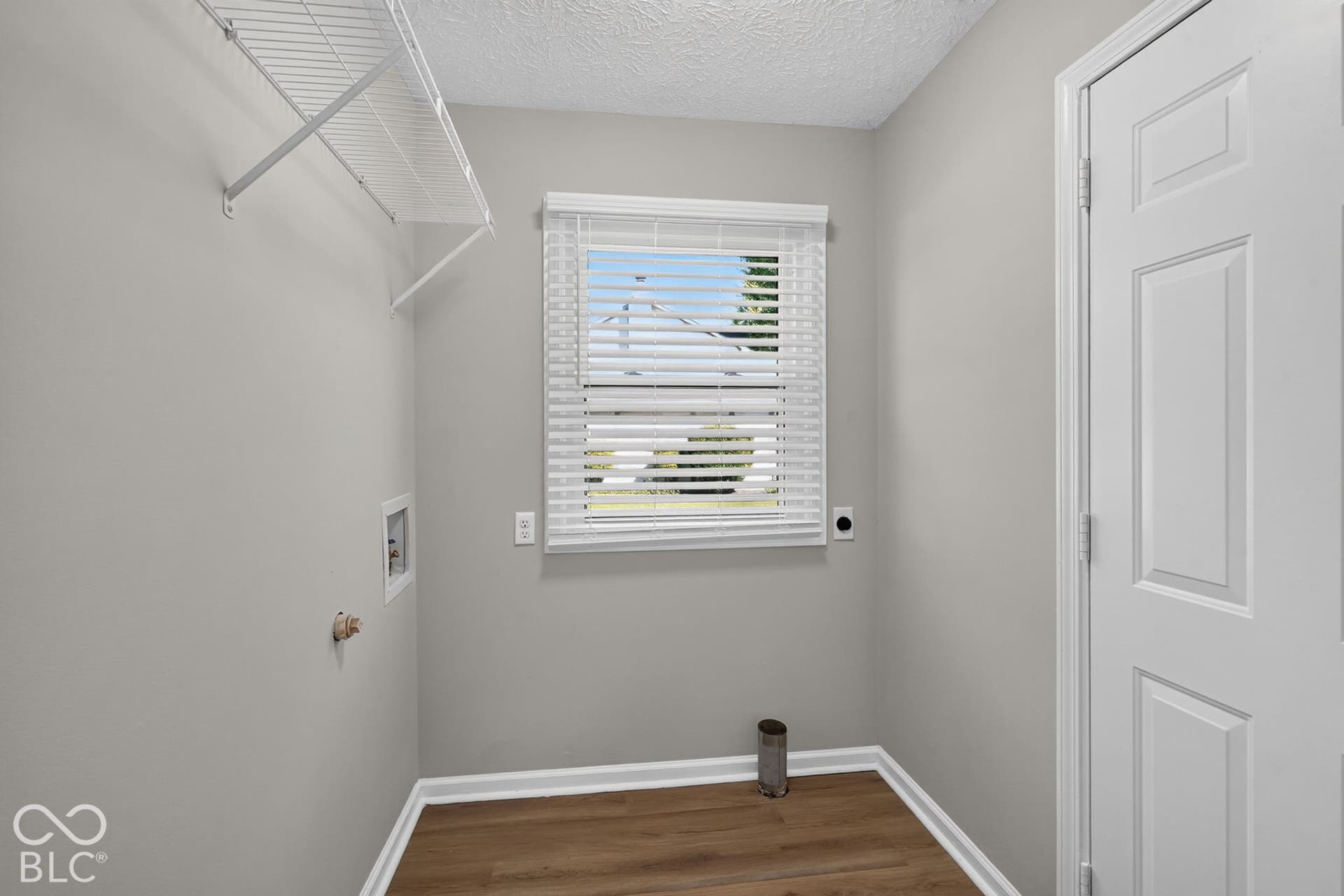 Utility space featuring wood-finish flooring, a single window with blinds, and white wire shelving