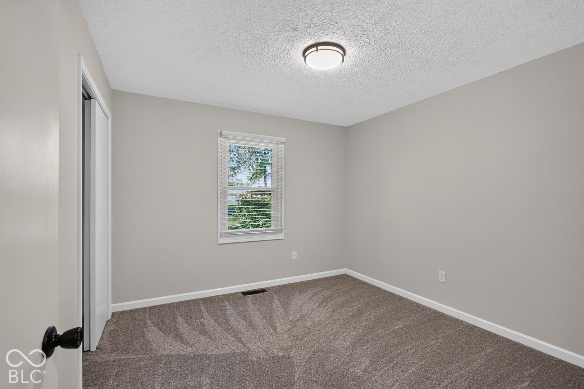 Textured carpeting, neutral wall color, and a single window with blinds