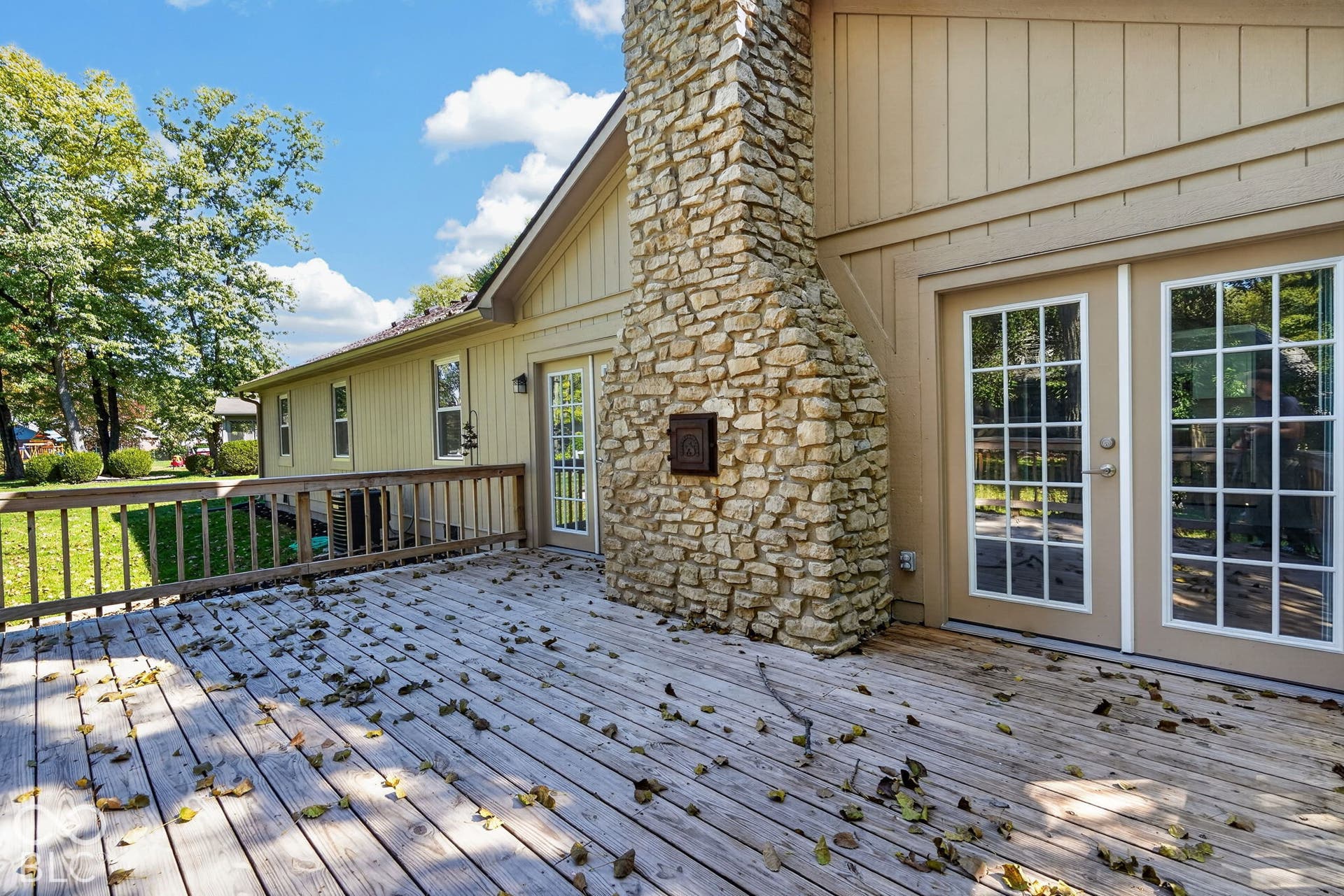 Expansive outdoor deck with a stone-clad chimney and direct access through double French doors