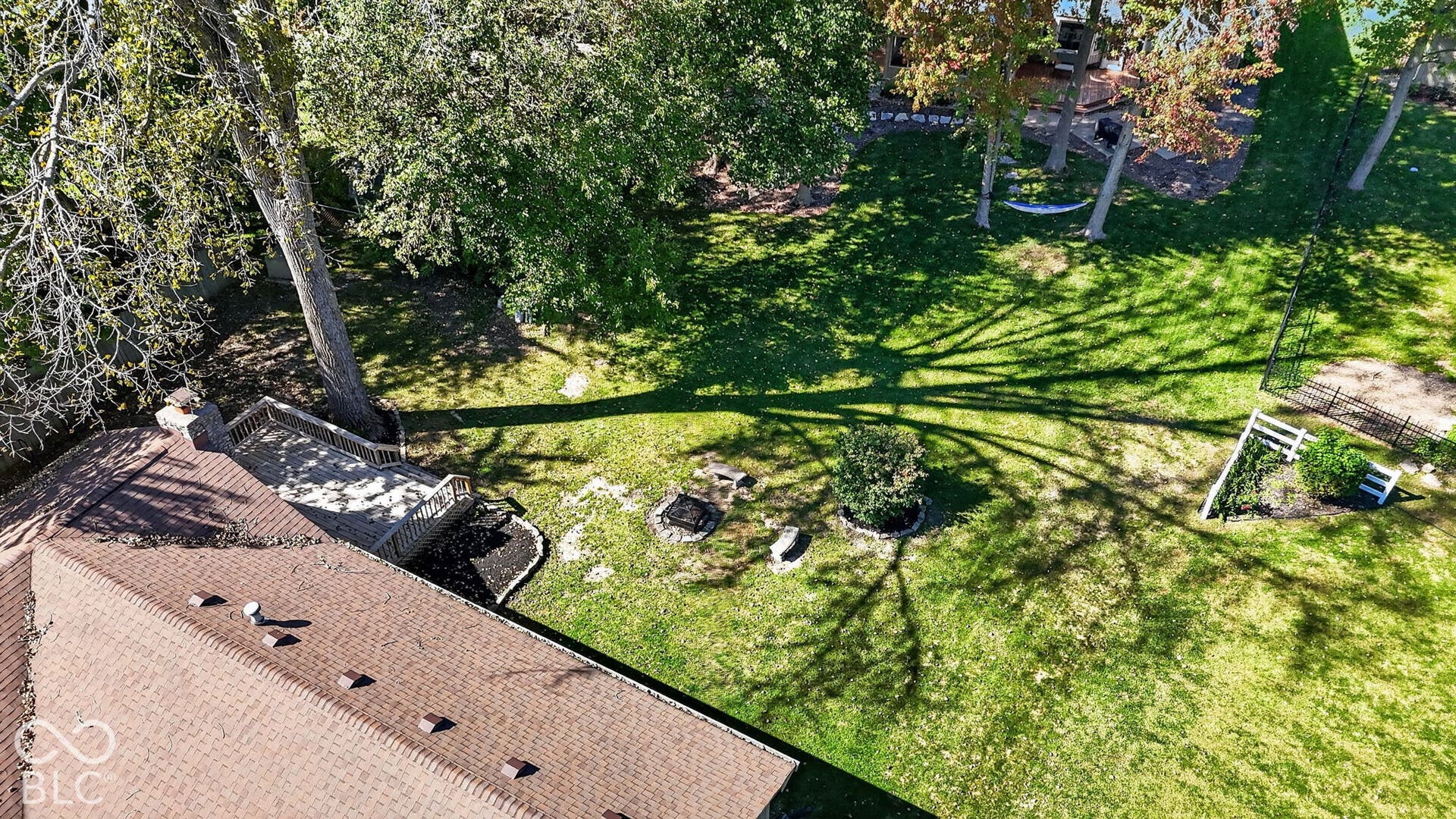 Expansive rear yard featuring green lawn, mature trees, and a built-in fire pit