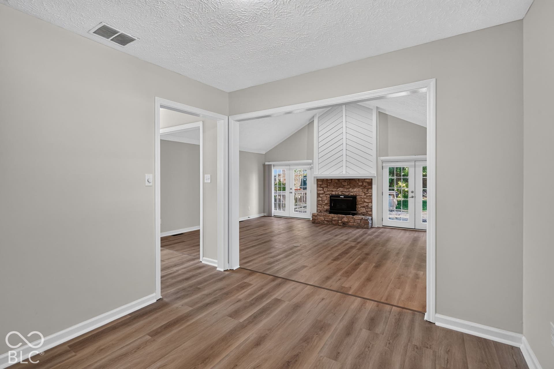 Vaulted ceiling with exposed beam, stone fireplace with hearth, wood-finish flooring, and French doors