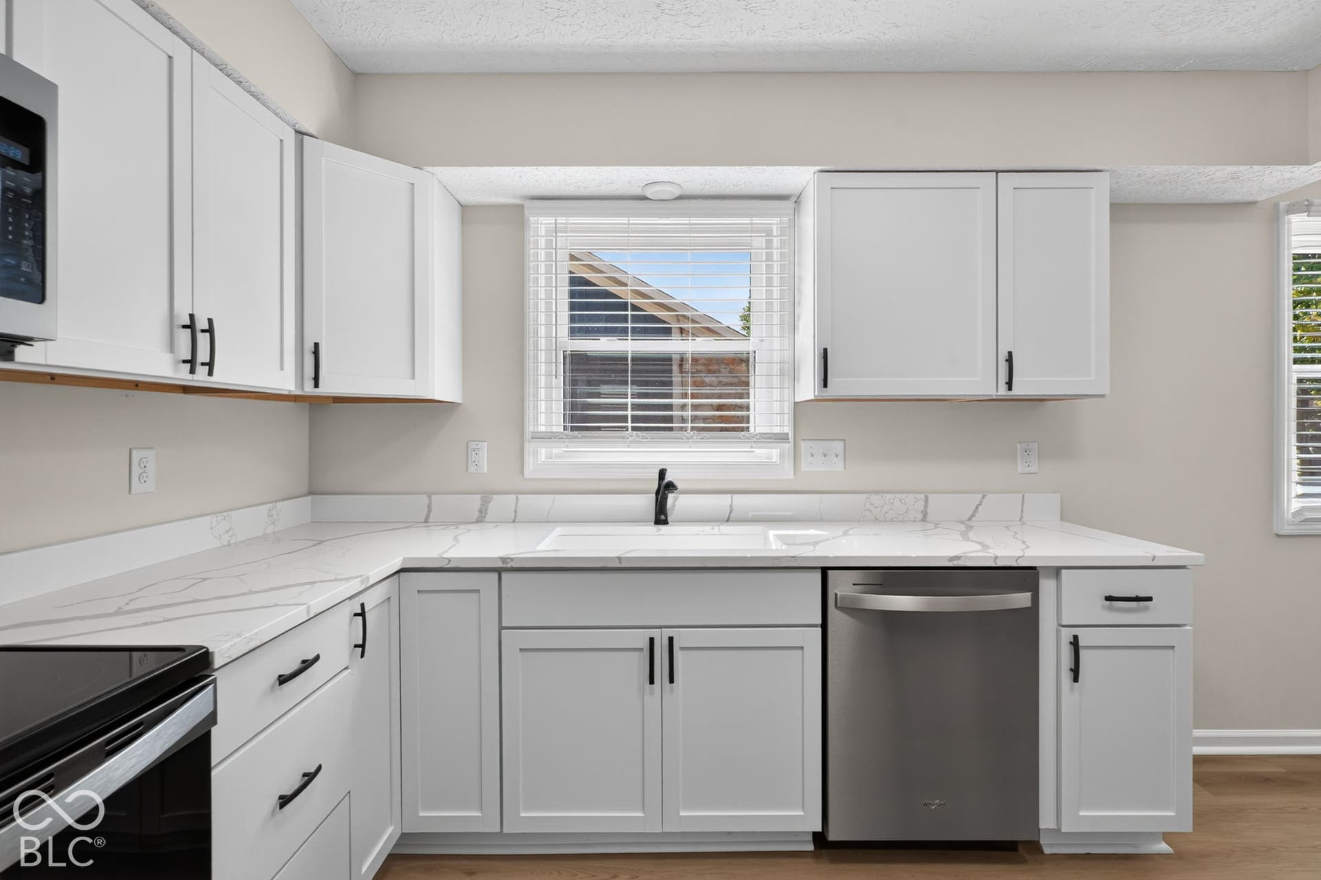 White shaker-style cabinetry, stainless steel dishwasher, quartz-finish countertops, undermount sink, and wood-finish flooring