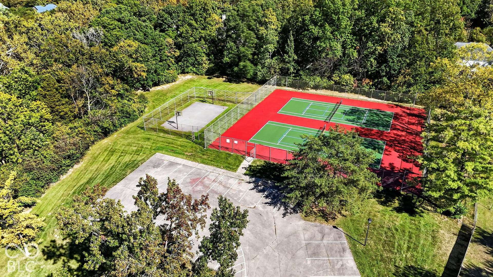 Two hard surface tennis courts with nets, a fenced basketball court, perimeter fencing, and mature trees