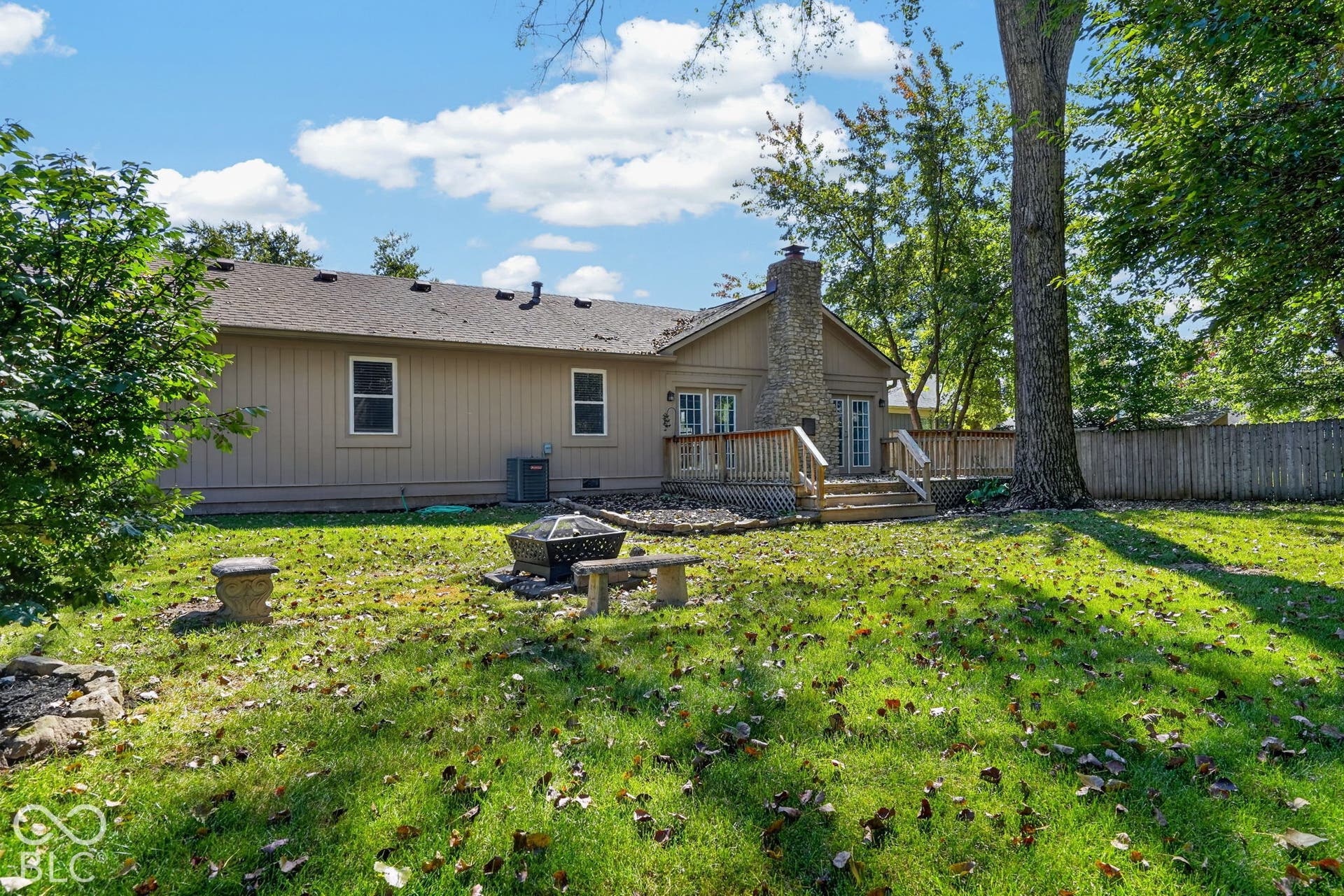 Expansive backyard with a manicured lawn, a stone-clad chimney, a wooden deck, and a privacy fence