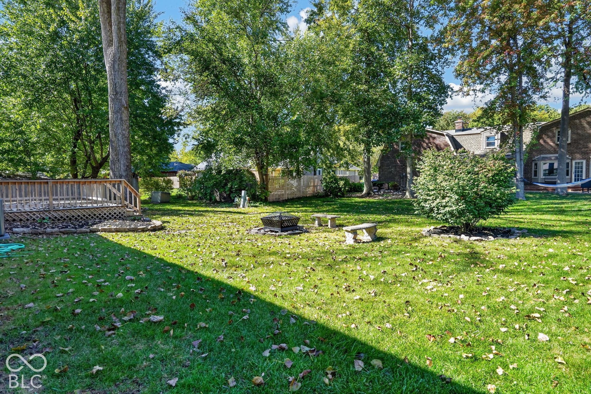 Expansive lawn featuring mature trees, a wood deck, a fire pit, and stone benches
