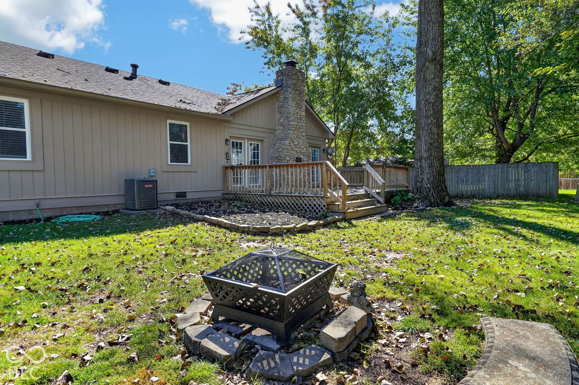 Expansive backyard featuring a wood deck, stone-faced chimney, and a stone-ringed fire pit