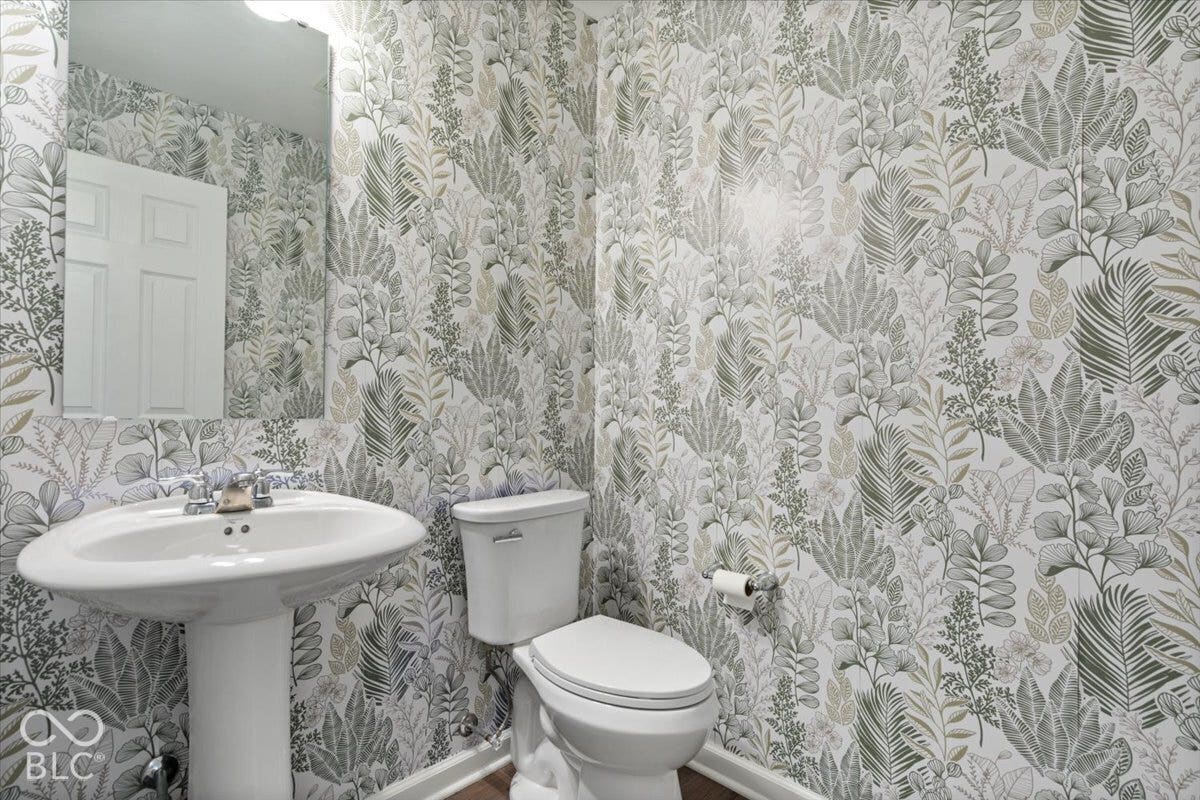 5570 W Stream Drive, McCordsville, IN 46055 Pedestal sink with chrome faucet, toilet, wall-mounted mirror, overhead lighting, and botanical wallpaper