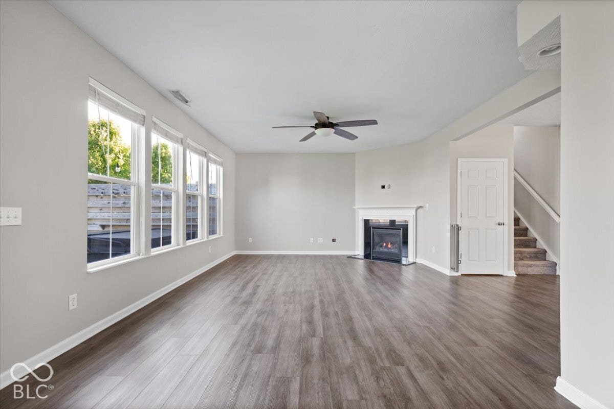5570 W Stream Drive, McCordsville, IN 46055 Spacious living area featuring wood-finish flooring, multiple windows, a ceiling fan, and a fireplace with a white mantel