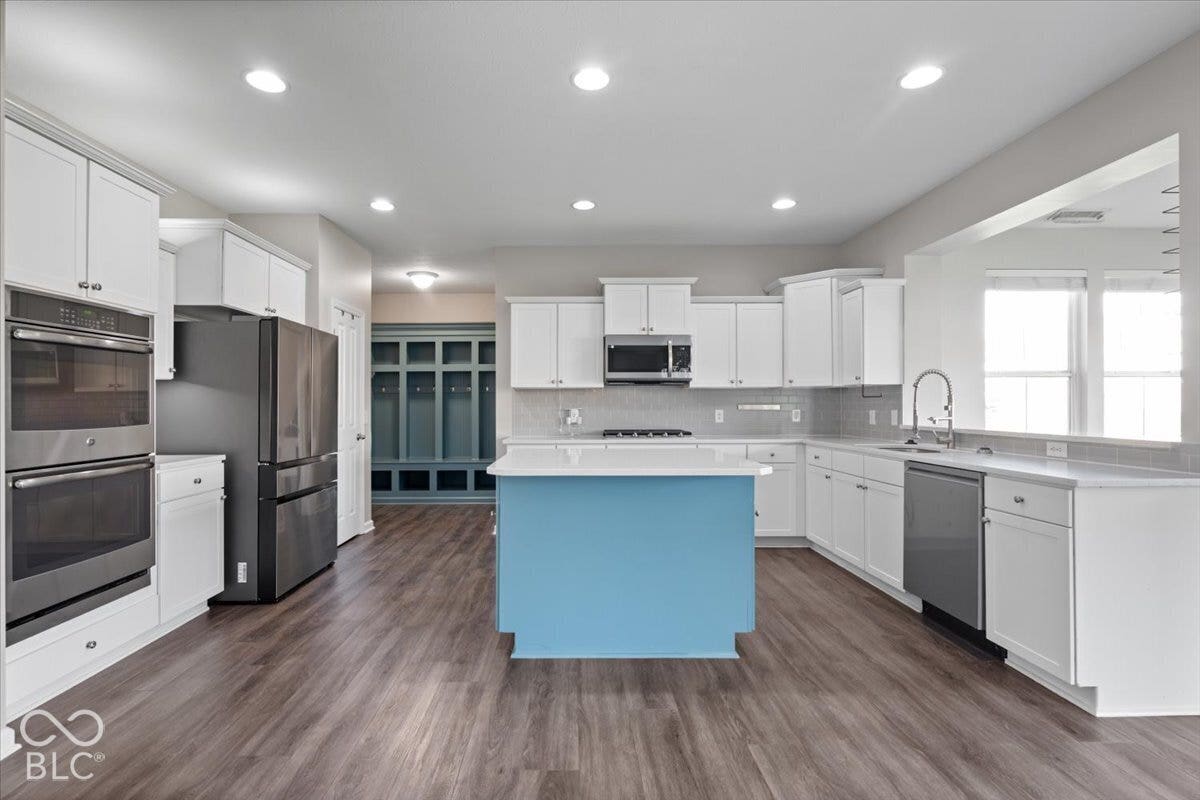 5570 W Stream Drive, McCordsville, IN 46055 Gourmet kitchen with double wall ovens, a blue-painted center island, wood-finish flooring, and white cabinetry