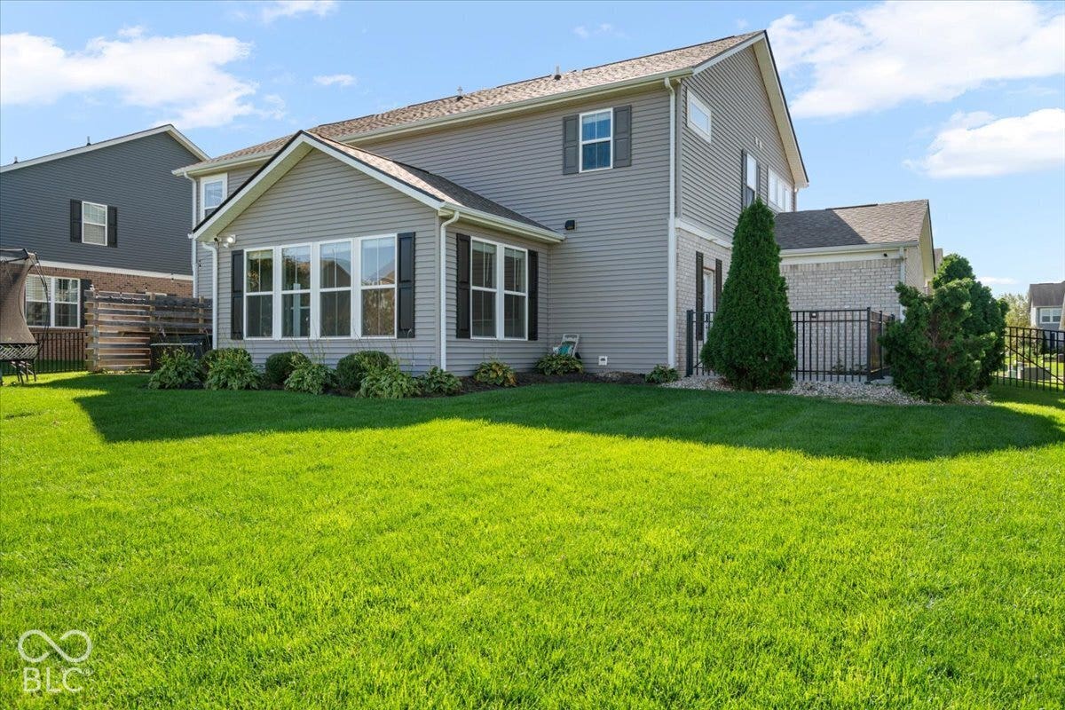 5570 W Stream Drive, McCordsville, IN 46055 Expansive backyard featuring a manicured lawn, a sunroom with multiple windows and black shutters, and mature landscaping
