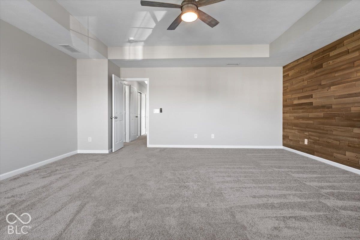 5570 W Stream Drive, McCordsville, IN 46055 Spacious room with tray ceiling, textured wood accent wall, and ceiling fan