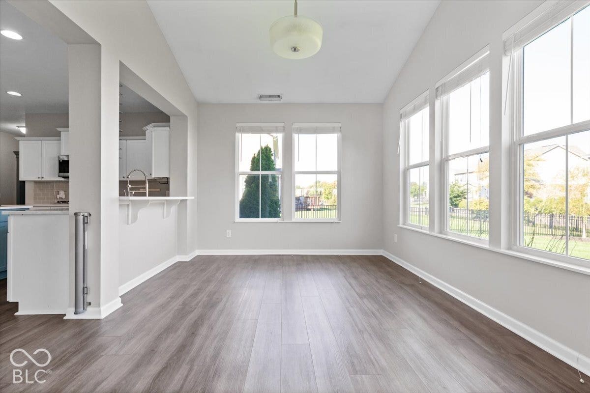 5570 W Stream Drive, McCordsville, IN 46055 Wood-finish flooring, vaulted ceiling, multiple large windows, and a pass-through counter to the kitchen featuring a stainless steel sink