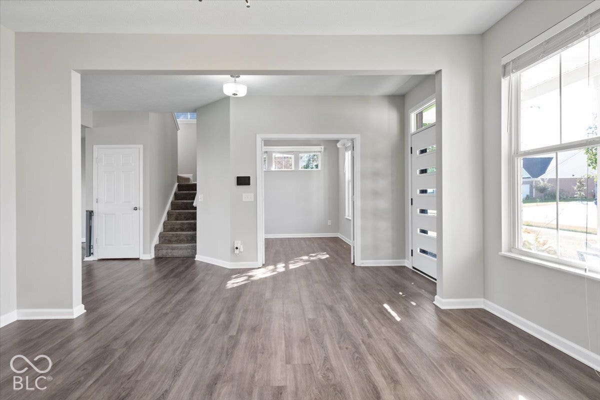 5570 W Stream Drive, McCordsville, IN 46055 Wood-finish flooring throughout, modern entry door with frosted glass inserts, bright windows, and a carpeted staircase
