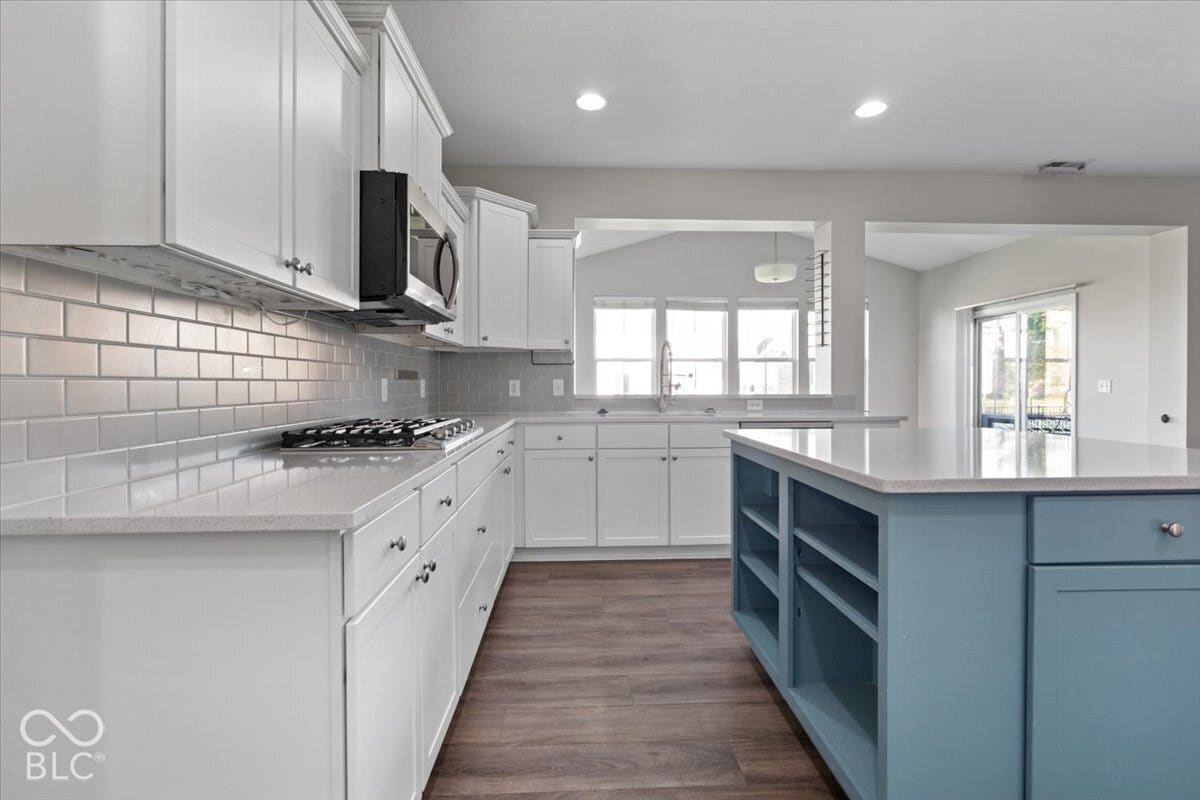 5570 W Stream Drive, McCordsville, IN 46055 White cabinetry, stainless steel microwave, gas cooktop, subway tile backsplash, and a contrasting blue island with integrated shelving