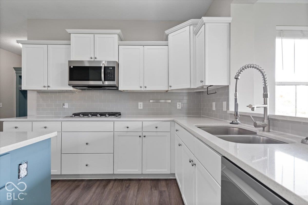5570 W Stream Drive, McCordsville, IN 46055 White shaker-style cabinetry with crown molding, stainless steel microwave, gas cooktop, subway tile backsplash, and a double basin sink with a high-arc faucet