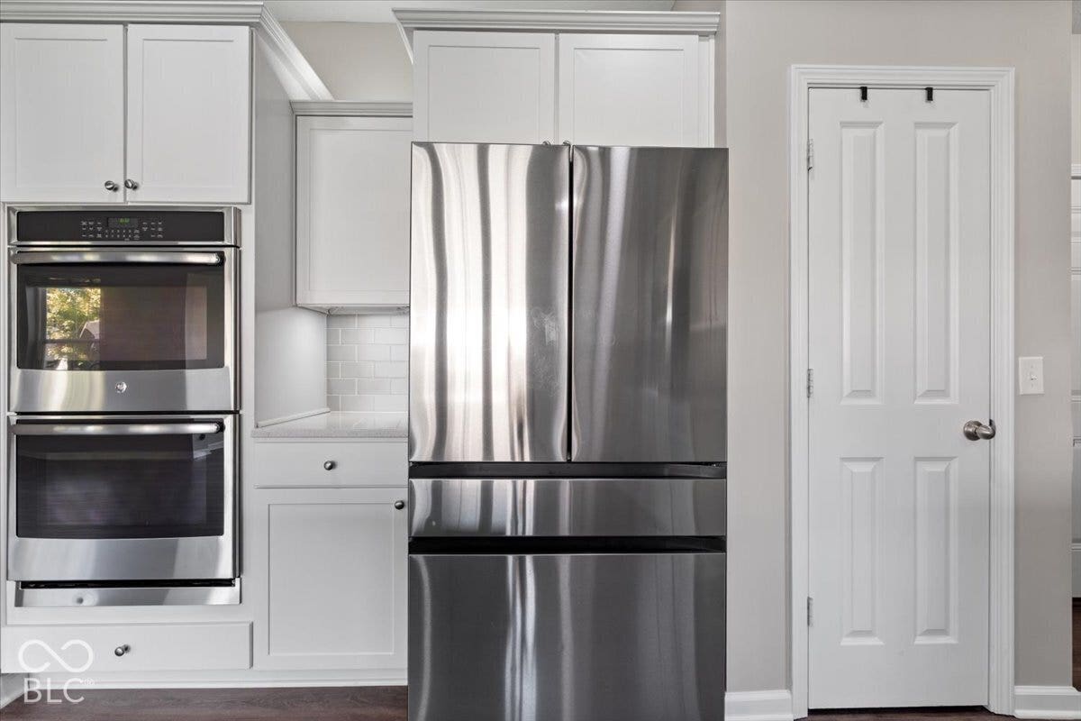 5570 W Stream Drive, McCordsville, IN 46055 White shaker-style cabinetry, stainless steel double oven, stainless steel French door refrigerator, subway tile backsplash, and light-toned countertop
