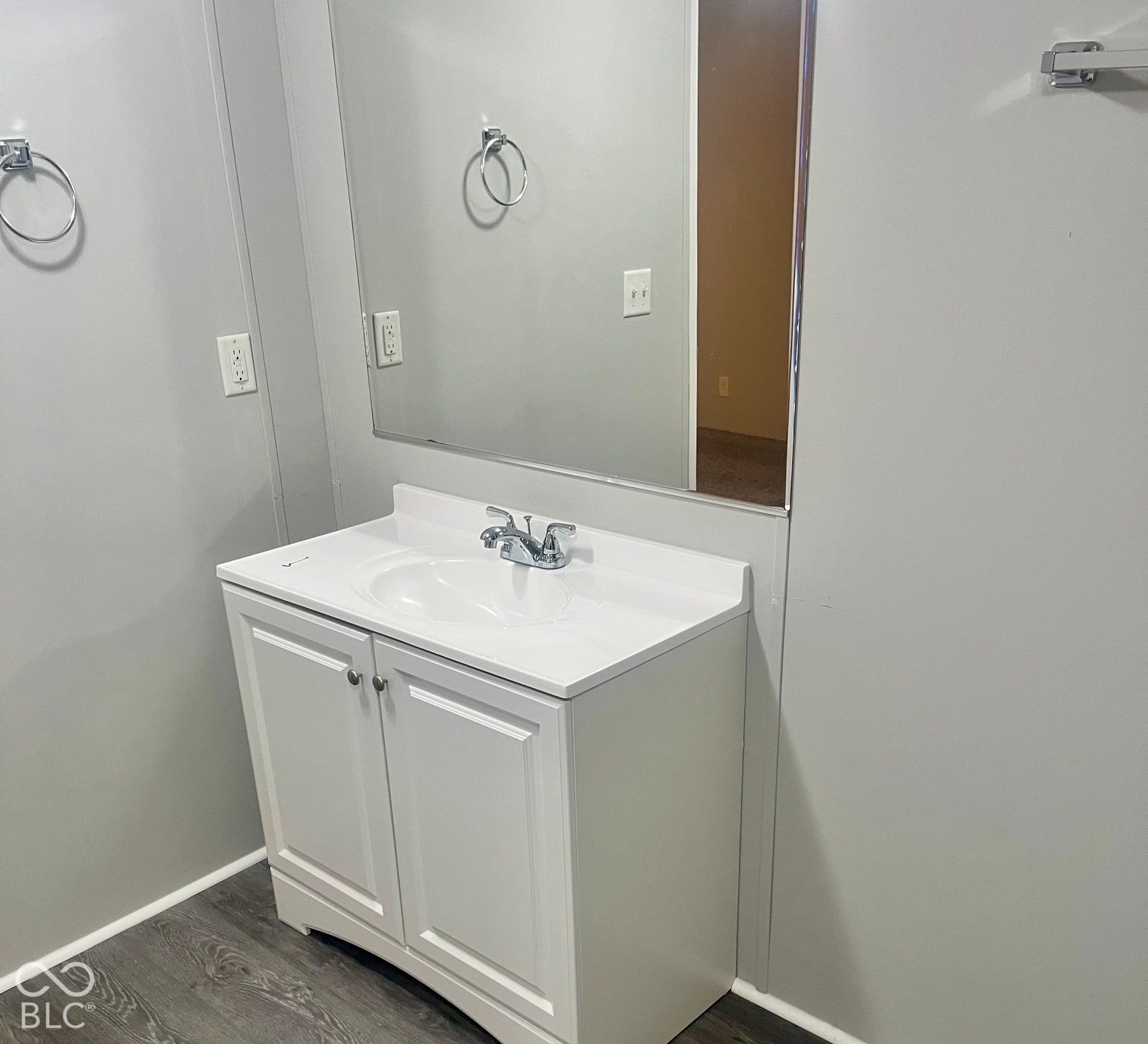 White vanity with integrated sink, chrome faucet, and wood-finish flooring