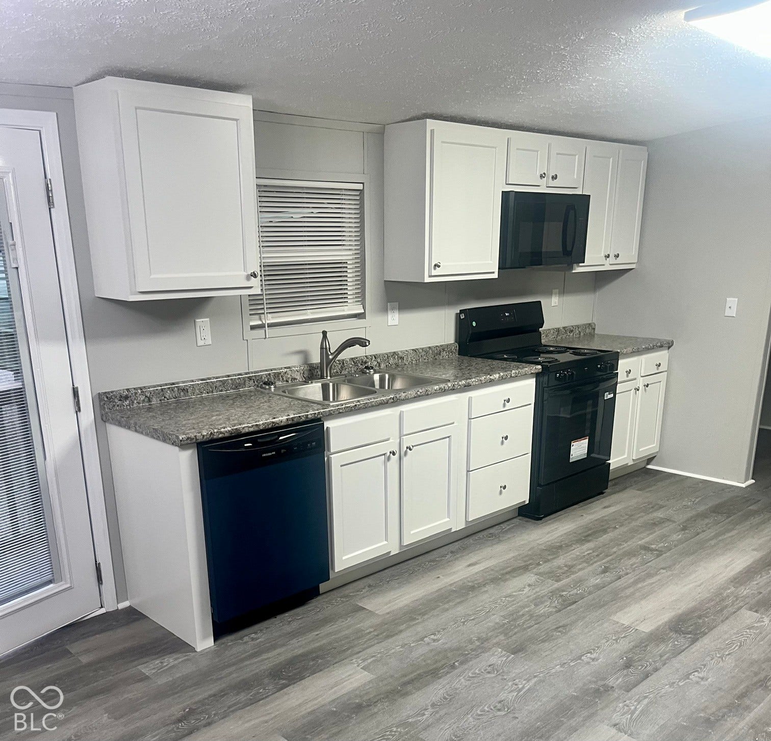 Kitchen featuring wood-finish flooring, white cabinetry, a double basin stainless steel sink, a black electric range, and a black dishwasher