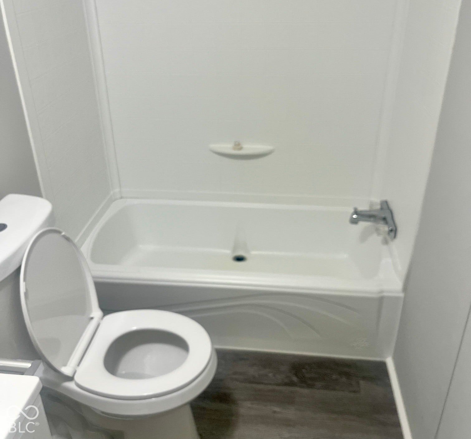 Bathtub with integrated shower surround, white ceramic toilet, and wood-finish flooring