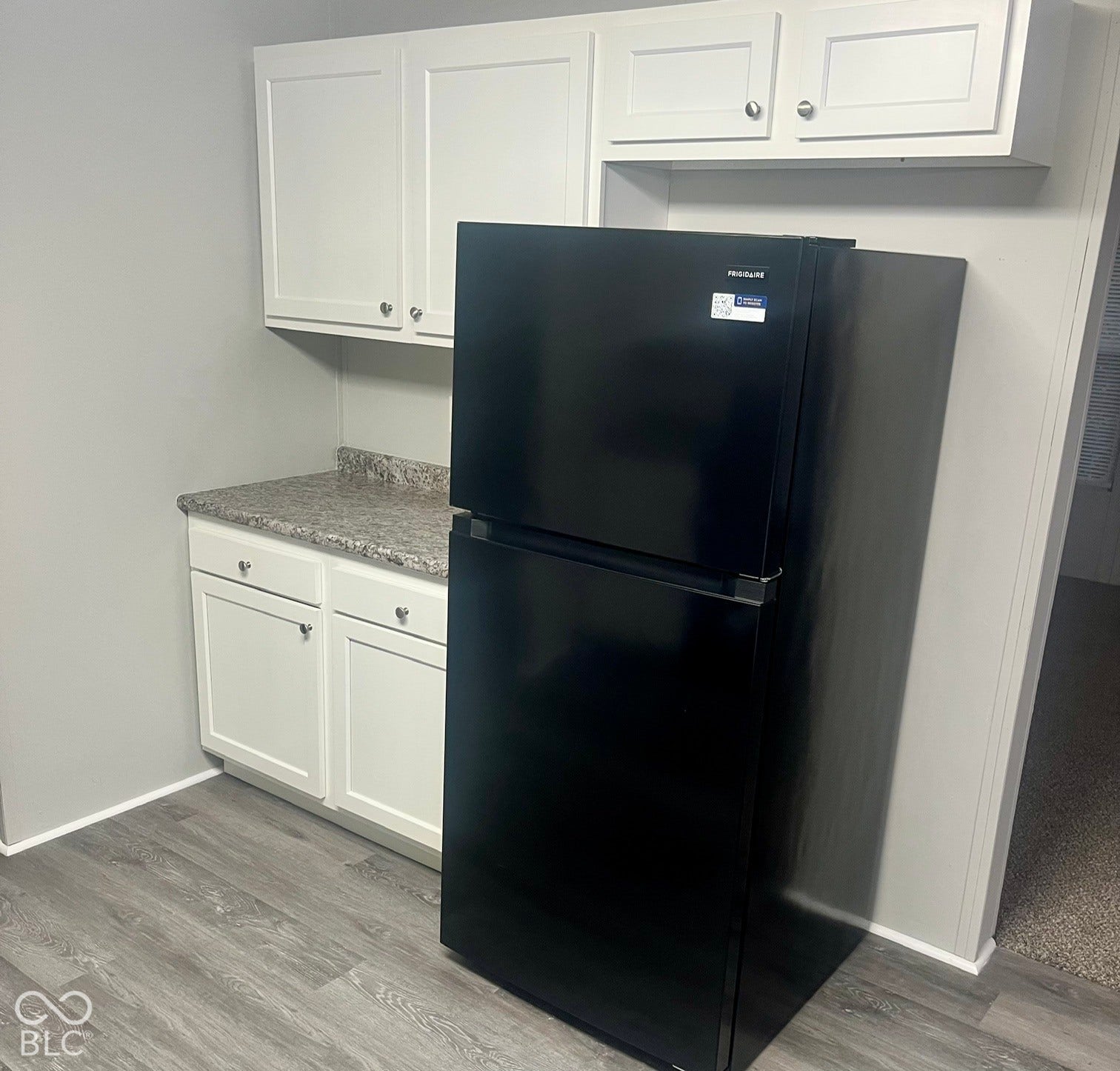 Modern kitchen space featuring white shaker-style cabinetry with chrome hardware, speckled countertops, and wood-finish flooring