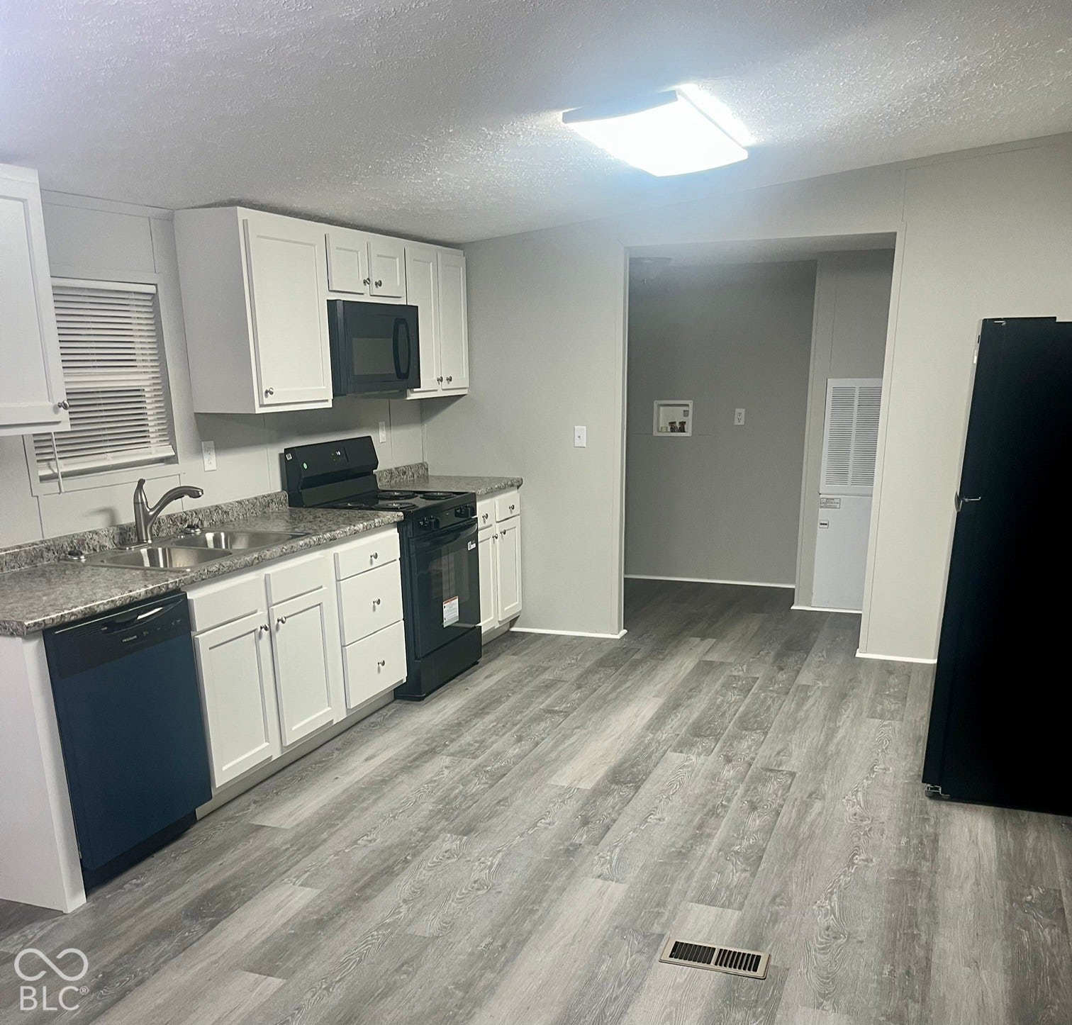 Kitchen featuring white cabinetry, gray countertops, wood-finish flooring, a stainless steel sink, and a black appliance suite
