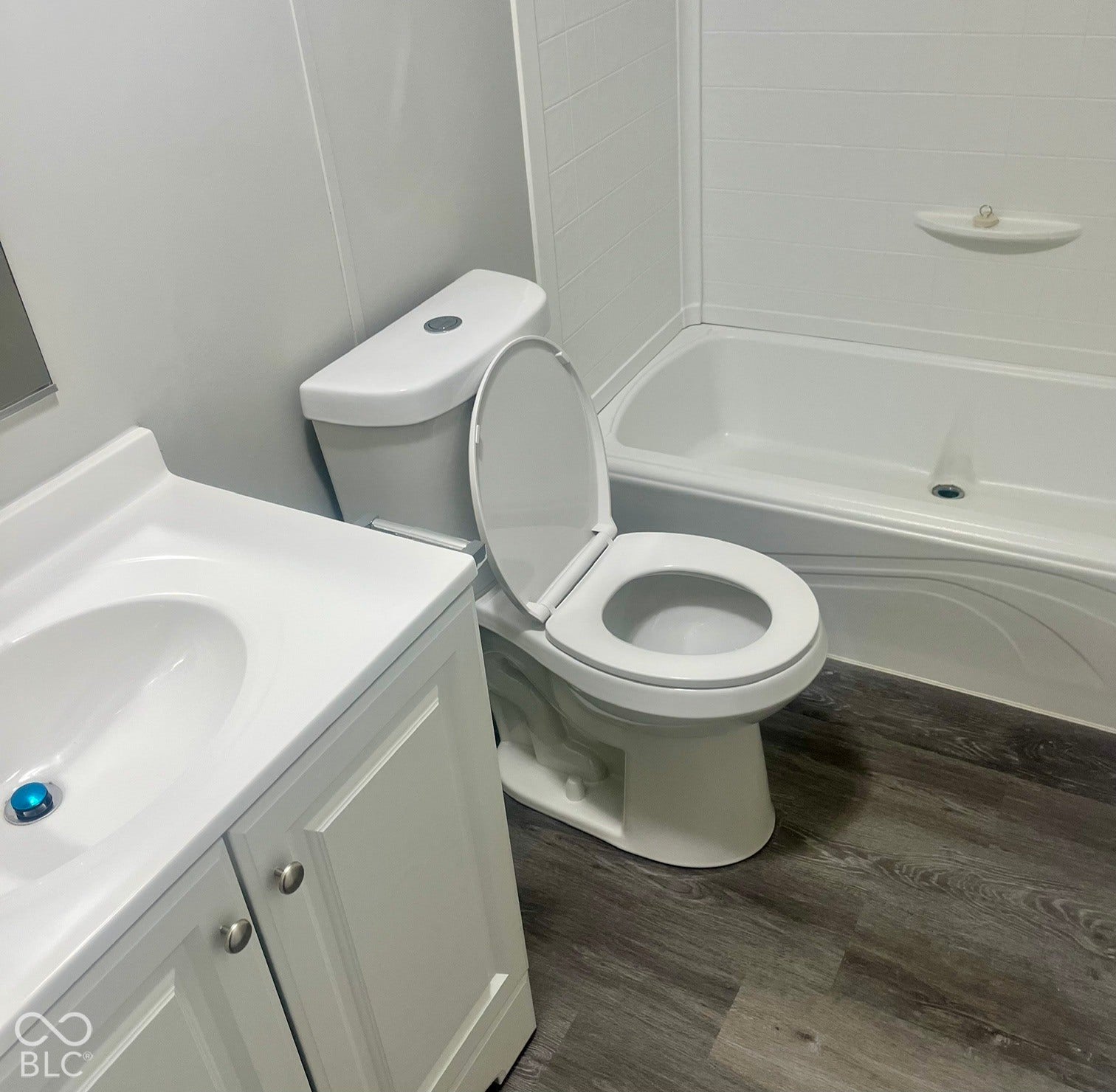 White vanity with integrated sink, toilet, bathtub with white surround, and wood-finish flooring