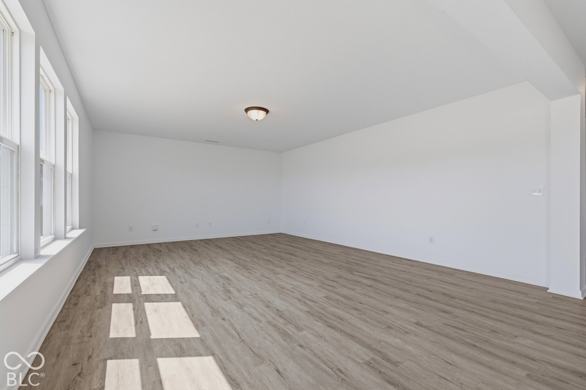 10525 Broadford Street, Indianapolis, IN 46239 Spacious room featuring multiple windows, wood-finish flooring, a neutral color palette, and a semi-flush mount ceiling light
