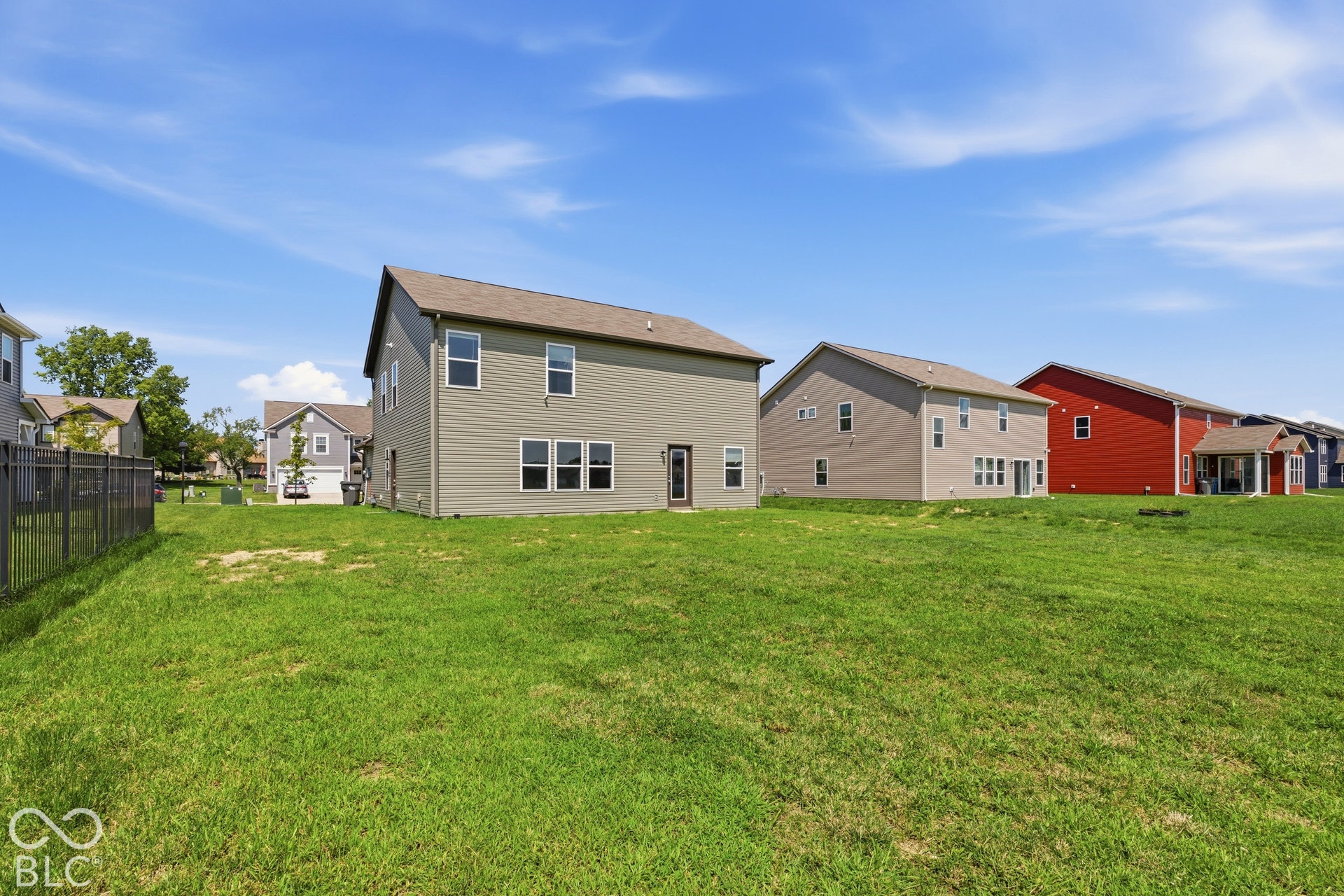 10525 Broadford Street, Indianapolis, IN 46239 Expansive green lawn with a chain-link fence bordering one side, leading to a two-story residence with light gray siding