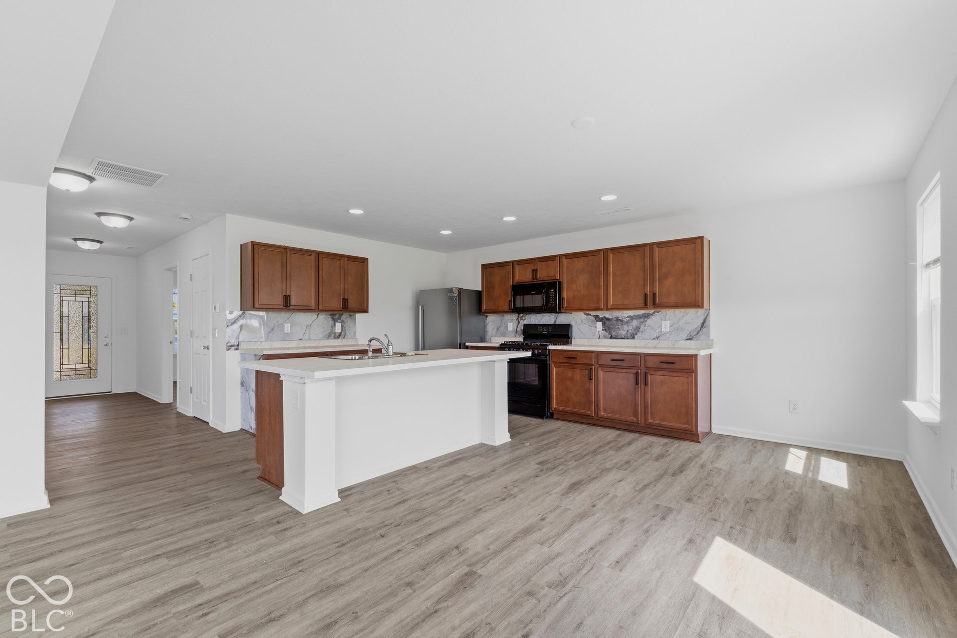 10525 Broadford Street, Indianapolis, IN 46239 Kitchen featuring wood-finish cabinetry, integrated stainless steel appliances, a center island with sink, and marble-look backsplash