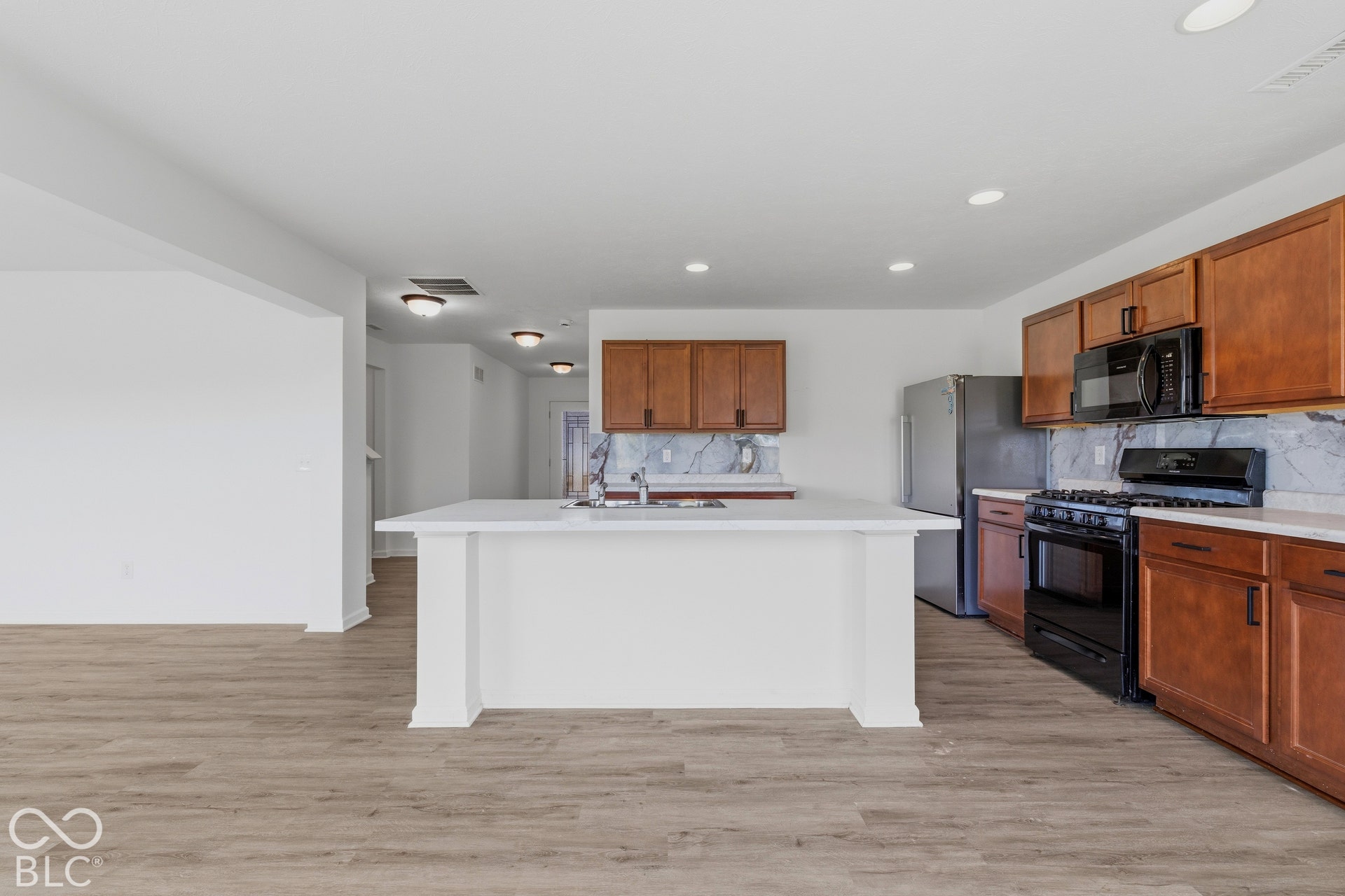 10525 Broadford Street, Indianapolis, IN 46239 Kitchen featuring wood-finish flooring, white countertops, a central island with an integrated sink, brown cabinetry, and stainless steel appliances