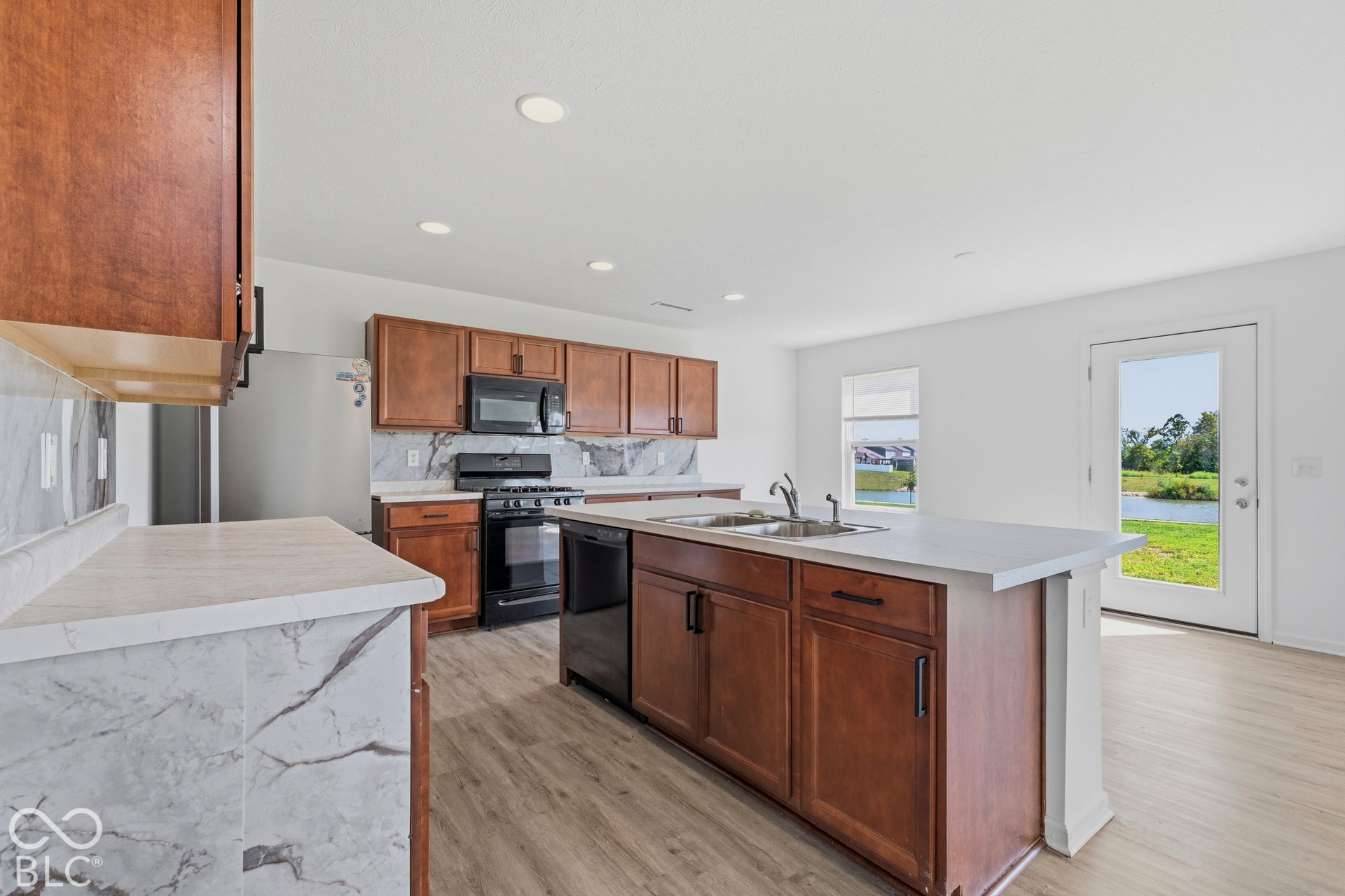 10525 Broadford Street, Indianapolis, IN 46239 Kitchen featuring wood-finish cabinetry, solid surface countertops, a center island with a double basin sink, and integrated black appliances