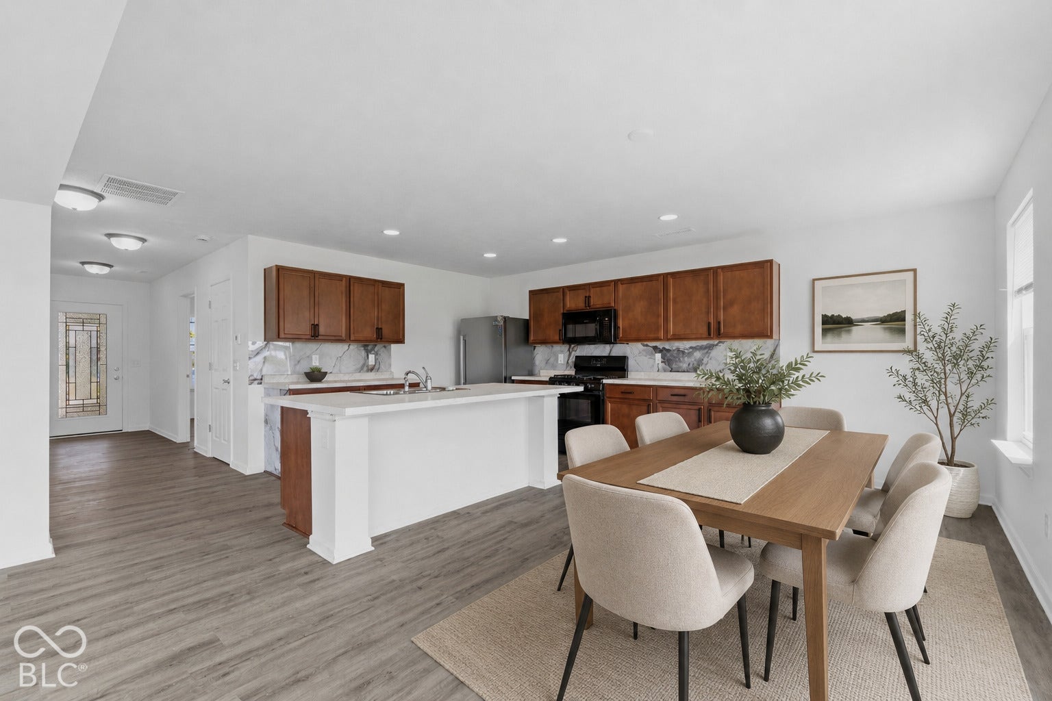 10525 Broadford Street, Indianapolis, IN 46239 Virtually Altered - Open-concept kitchen and dining area featuring wood-finish flooring, wood cabinetry, a white island with an integrated sink, and a window
