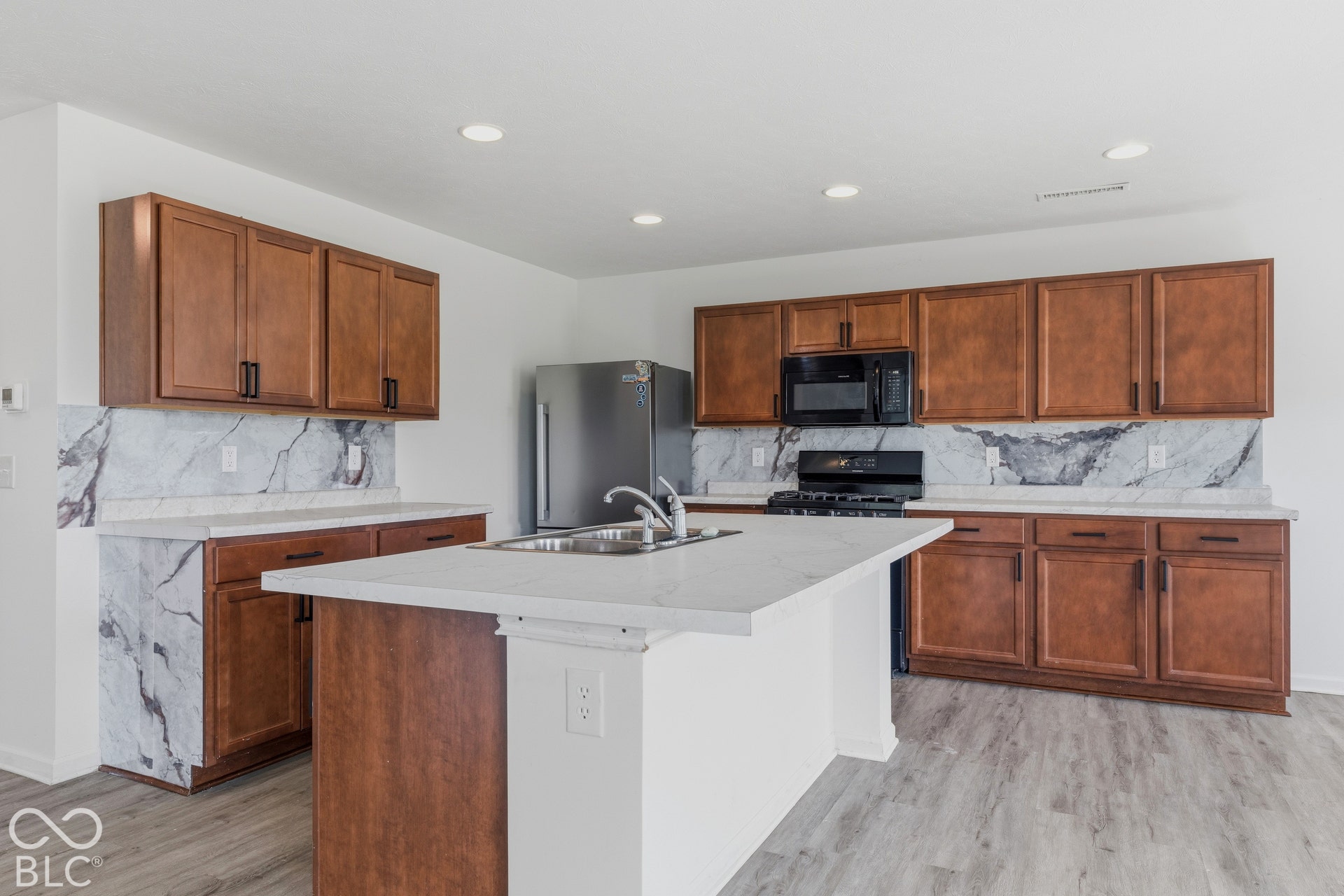 10525 Broadford Street, Indianapolis, IN 46239 Wood-finish cabinetry, light-toned countertops, tile backsplash with dark veining, black appliances, and a central island with an integrated sink