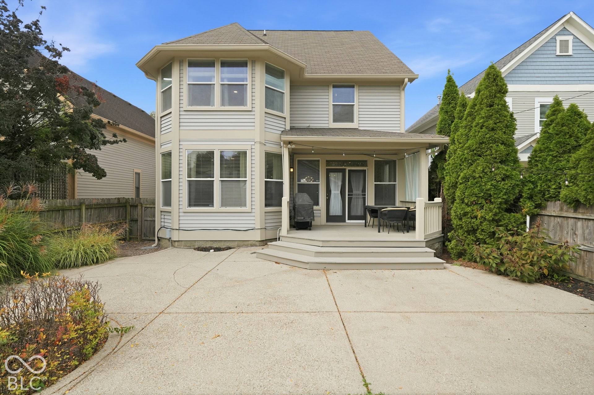 Two-story exterior with light-toned siding and multiple windows, featuring a multi-level deck with steps down to a concrete patio