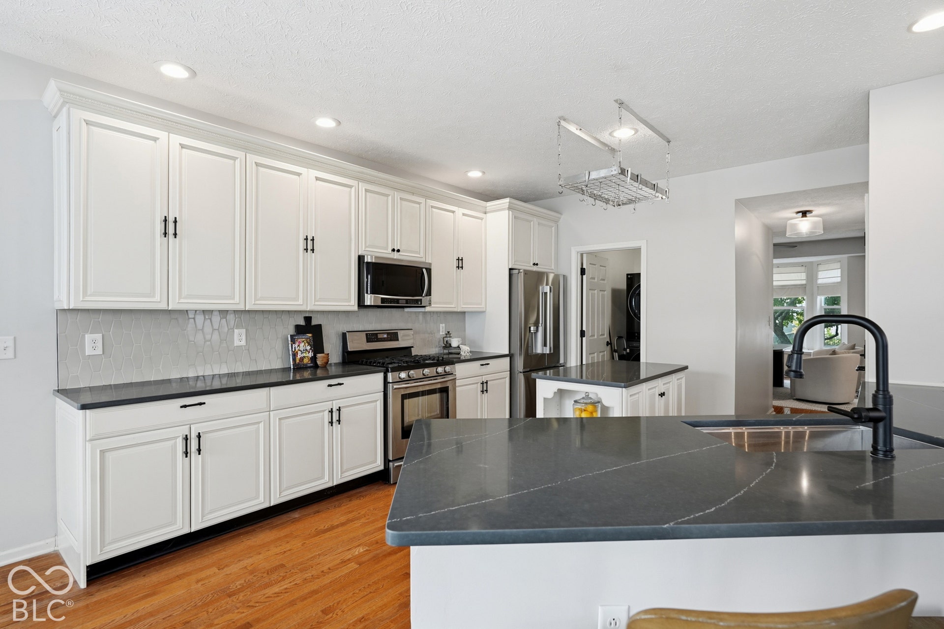 White cabinetry with black hardware, dark countertops, hexagonal tile backsplash, stainless steel appliances, and hardwood flooring