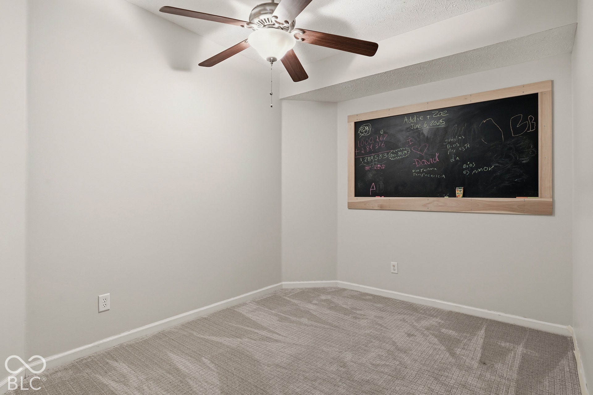 Built-in chalkboard with natural wood frame, ceiling fan with integrated lighting, and neutral carpeting
