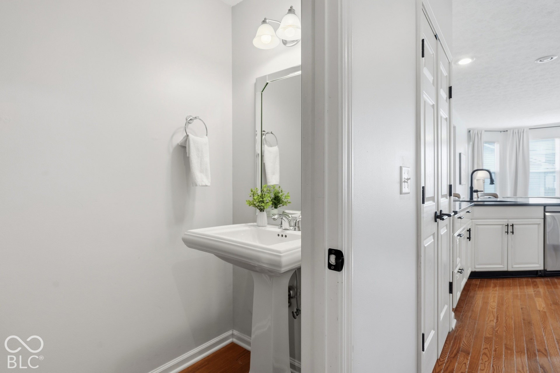Pedestal sink with chrome faucet, wall-mounted mirror with overhead vanity lighting, and hardwood flooring