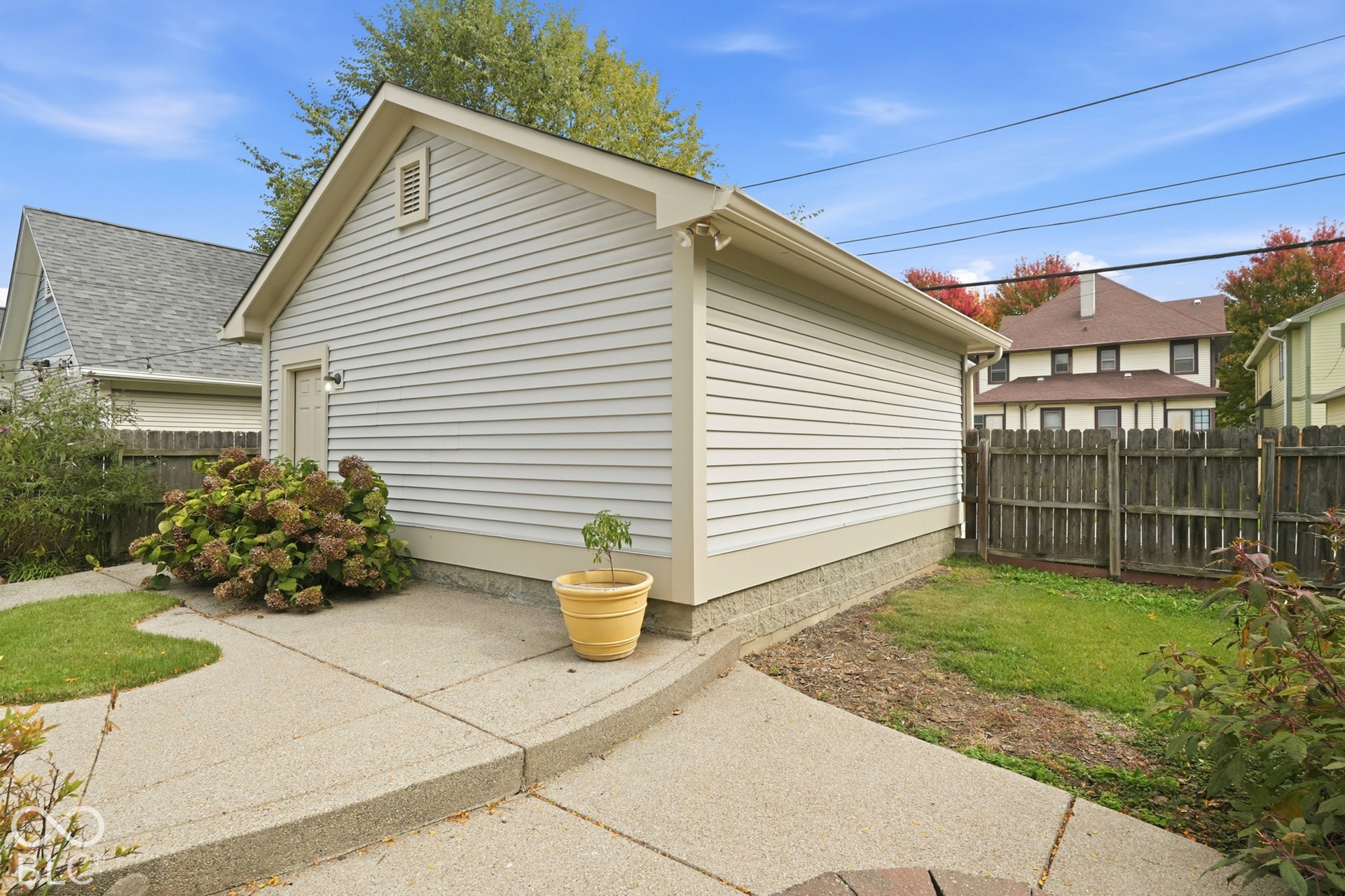 Detached garage with horizontal siding and a side entry door, featuring a concrete walkway and surrounding landscaping